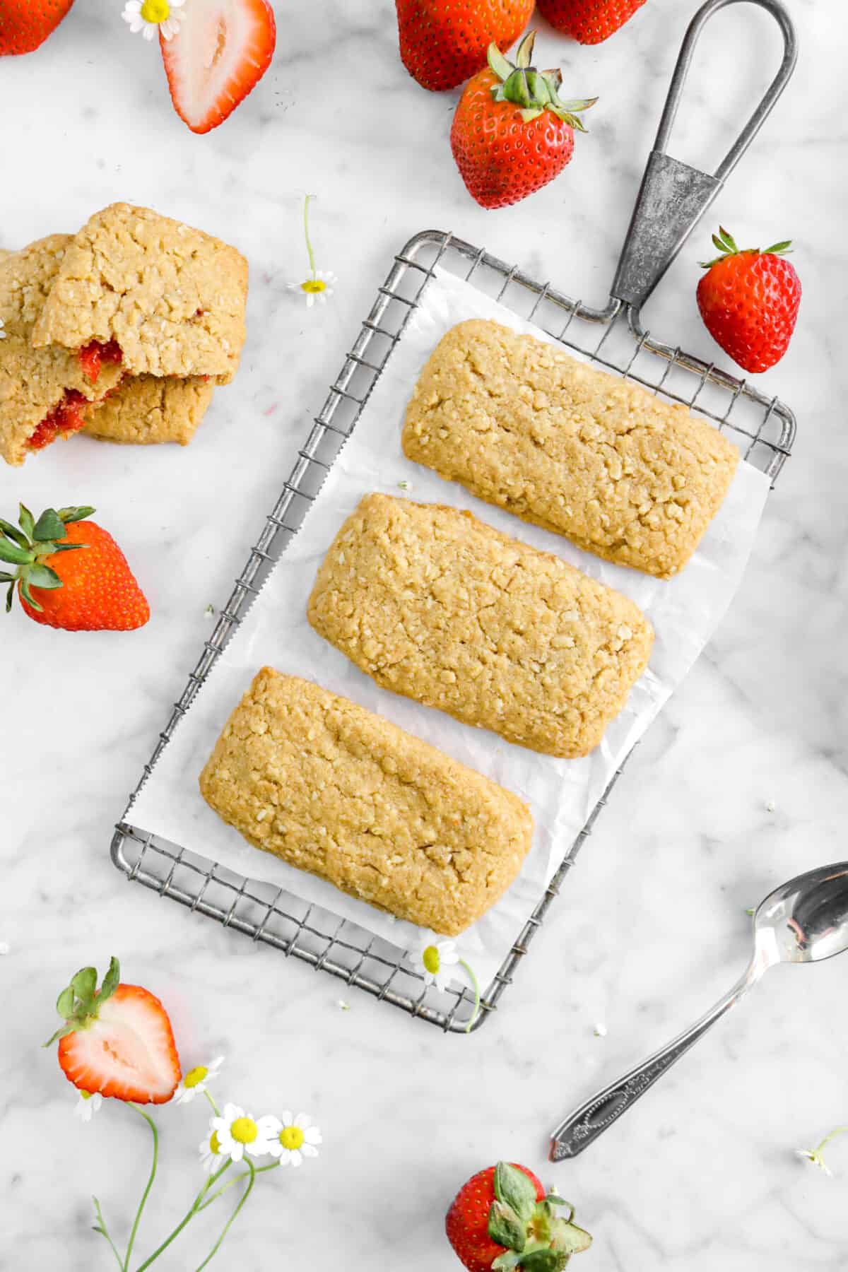 three nutri grain bars on wire cooling rack with strawberries, a spoon, chamomile flowers, and more nutri grain bars around