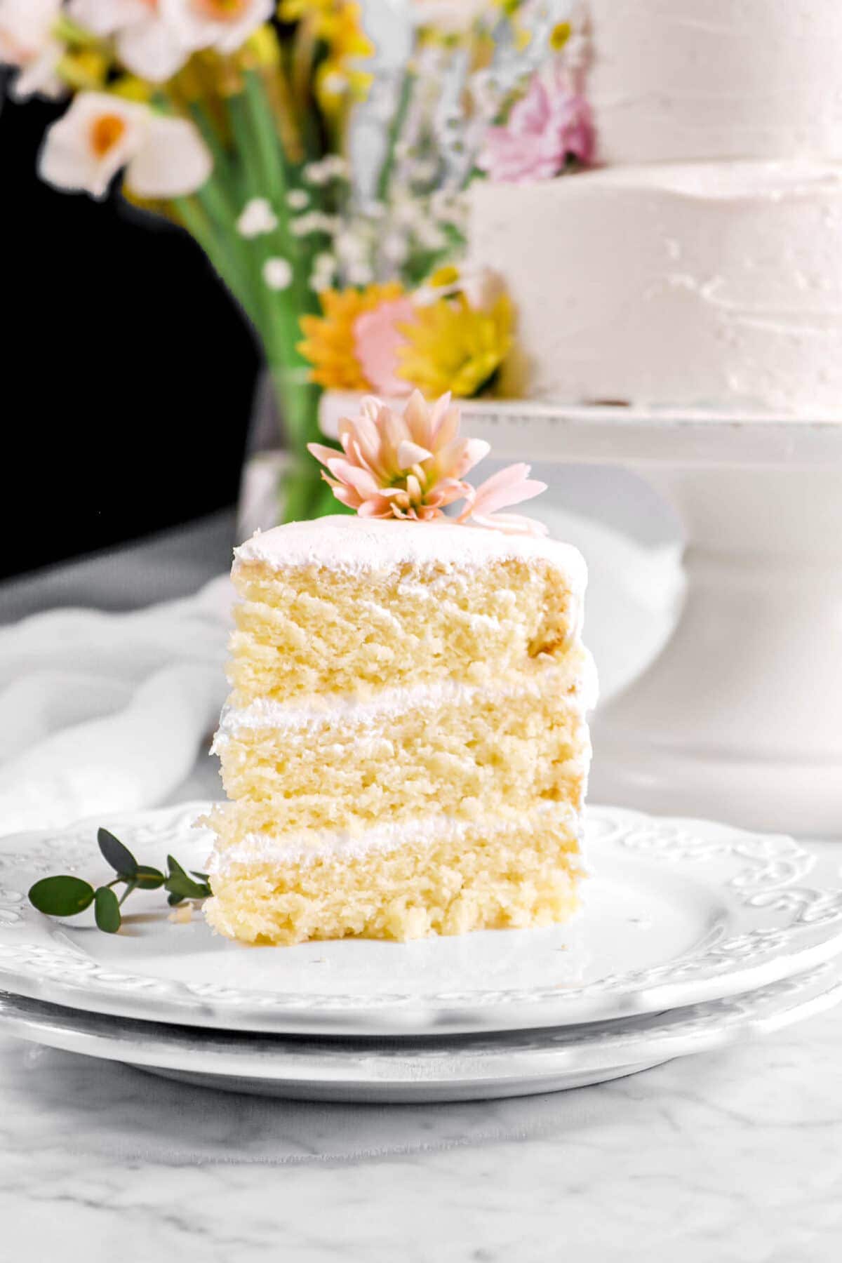 slice of vegan almond cake on two stacked plates with flowers behind