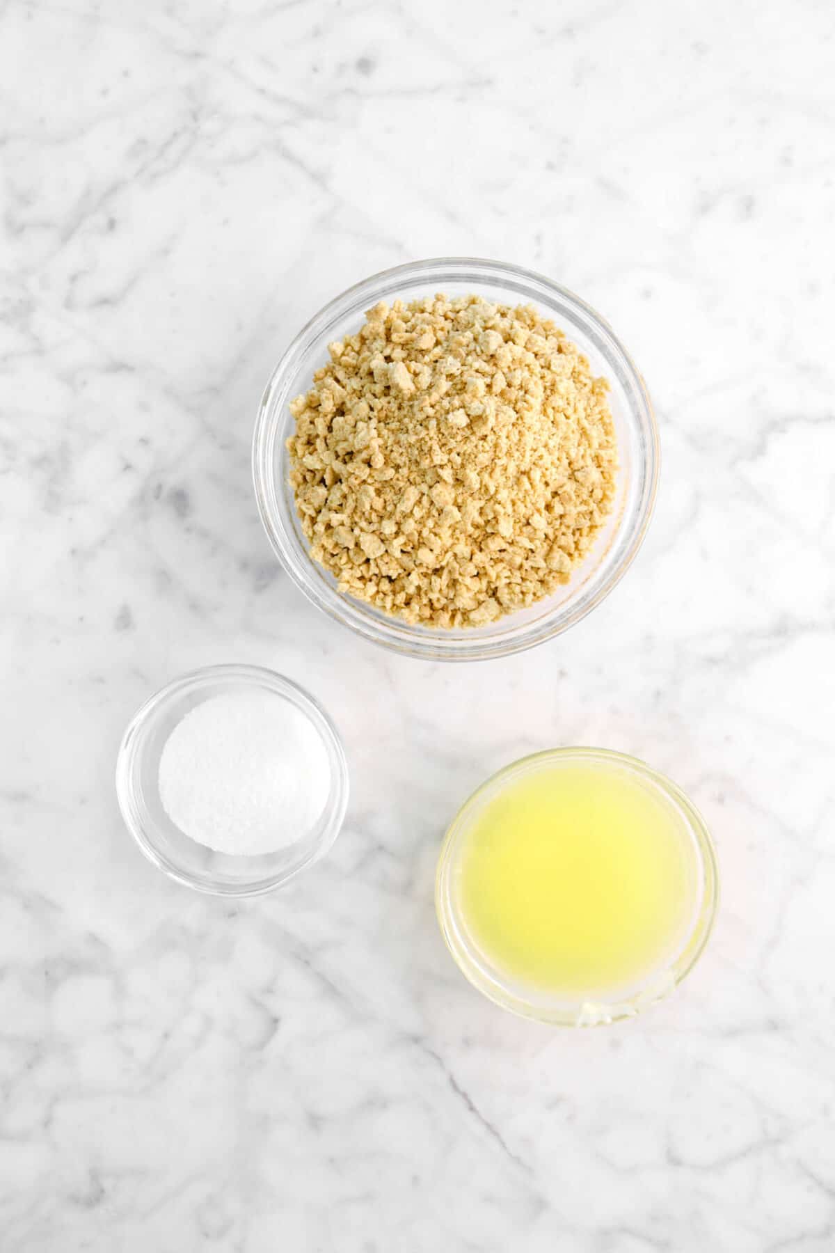 graham cracker crumbs, sugar, and melted butter in bowls on marble counter