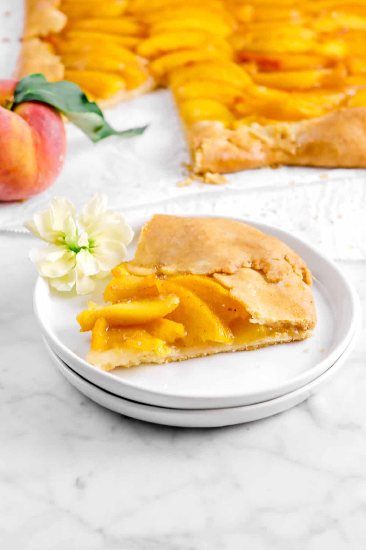 slice of peach galette on two white plates with a yellow flowers