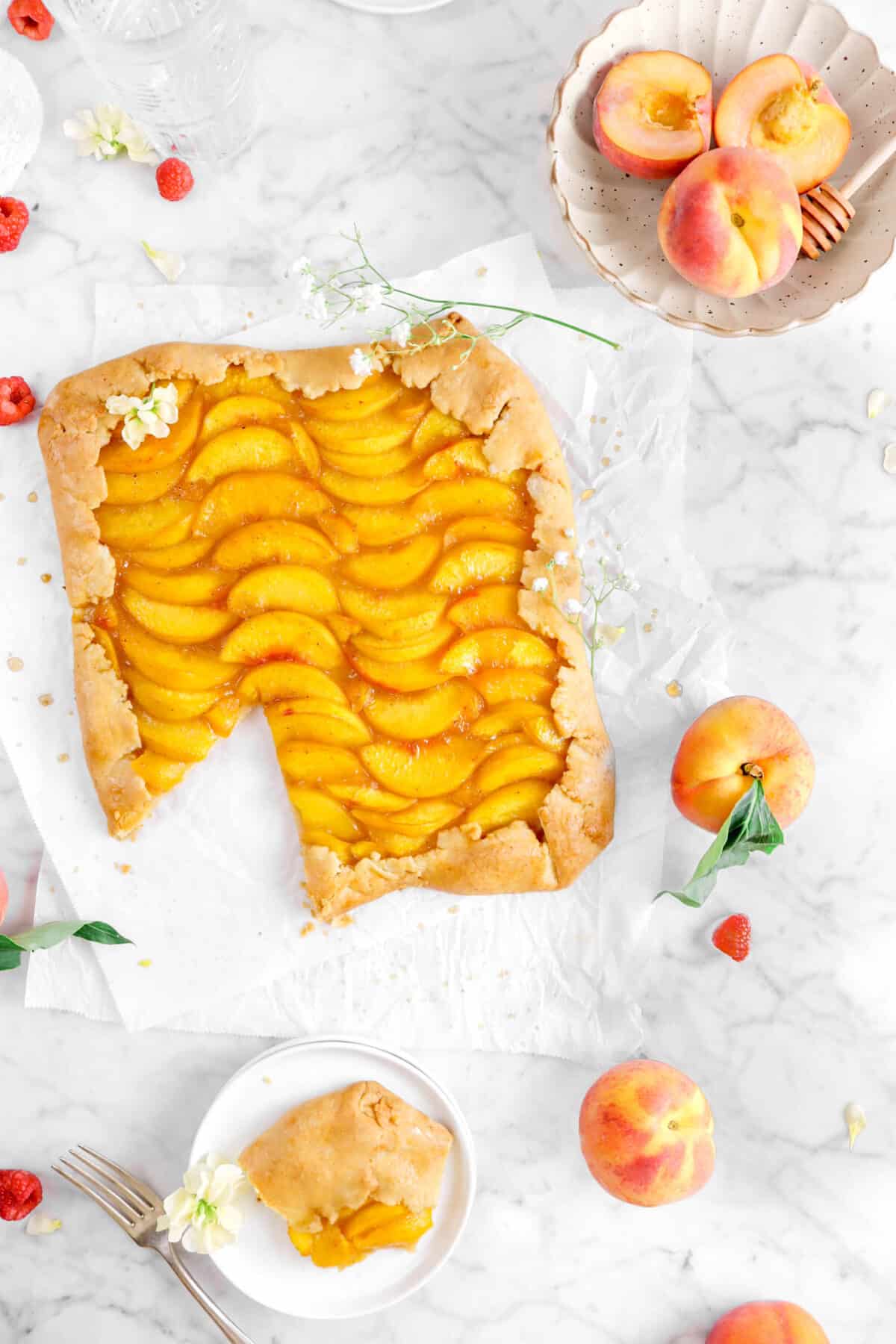 overhead shot of peach galette with slice on white plate, with flowers, and peaches around