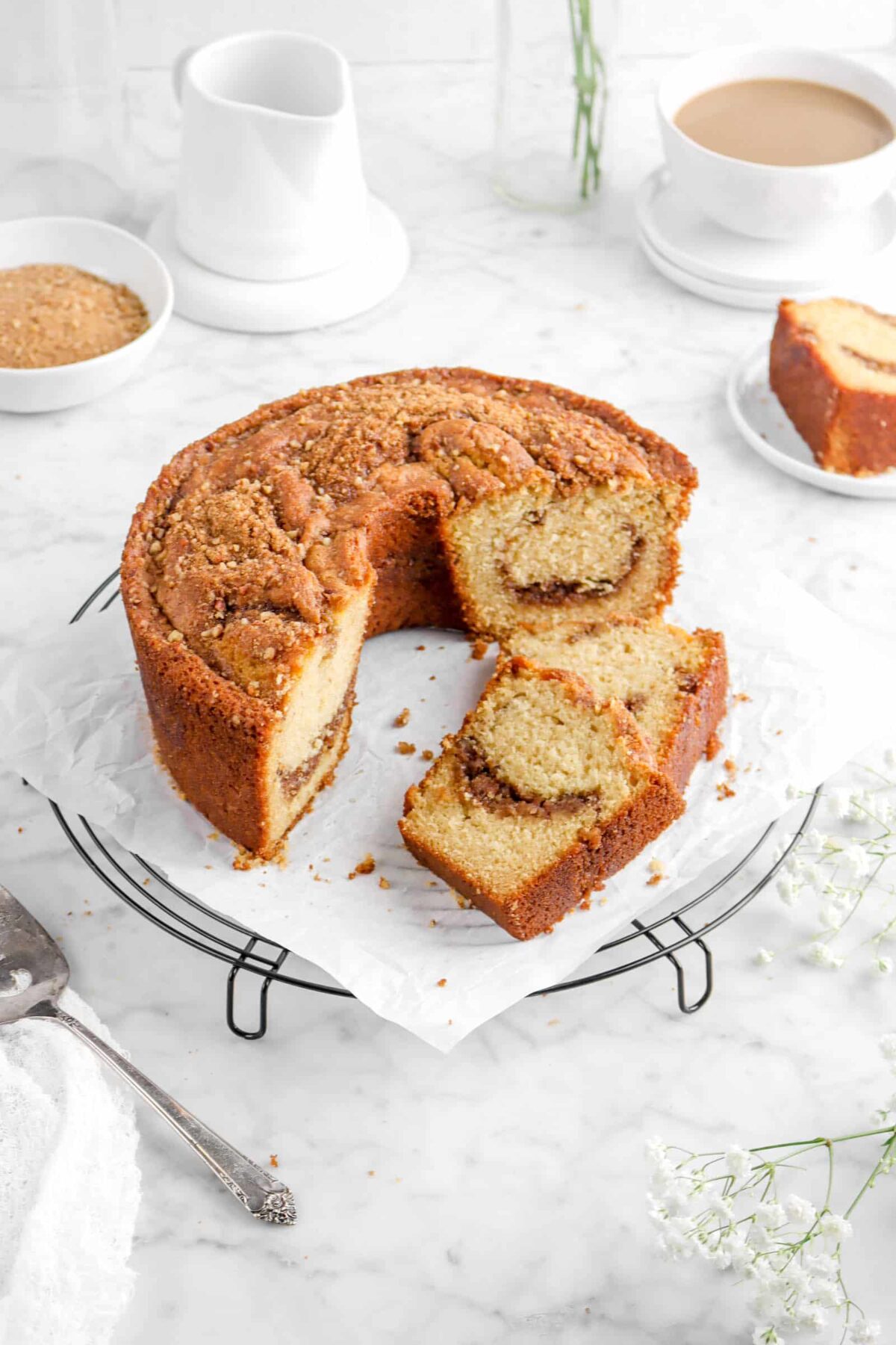 coffee cake with flowers, a cake knife, a cup of coffee, and a bowl of cinnamon streusel