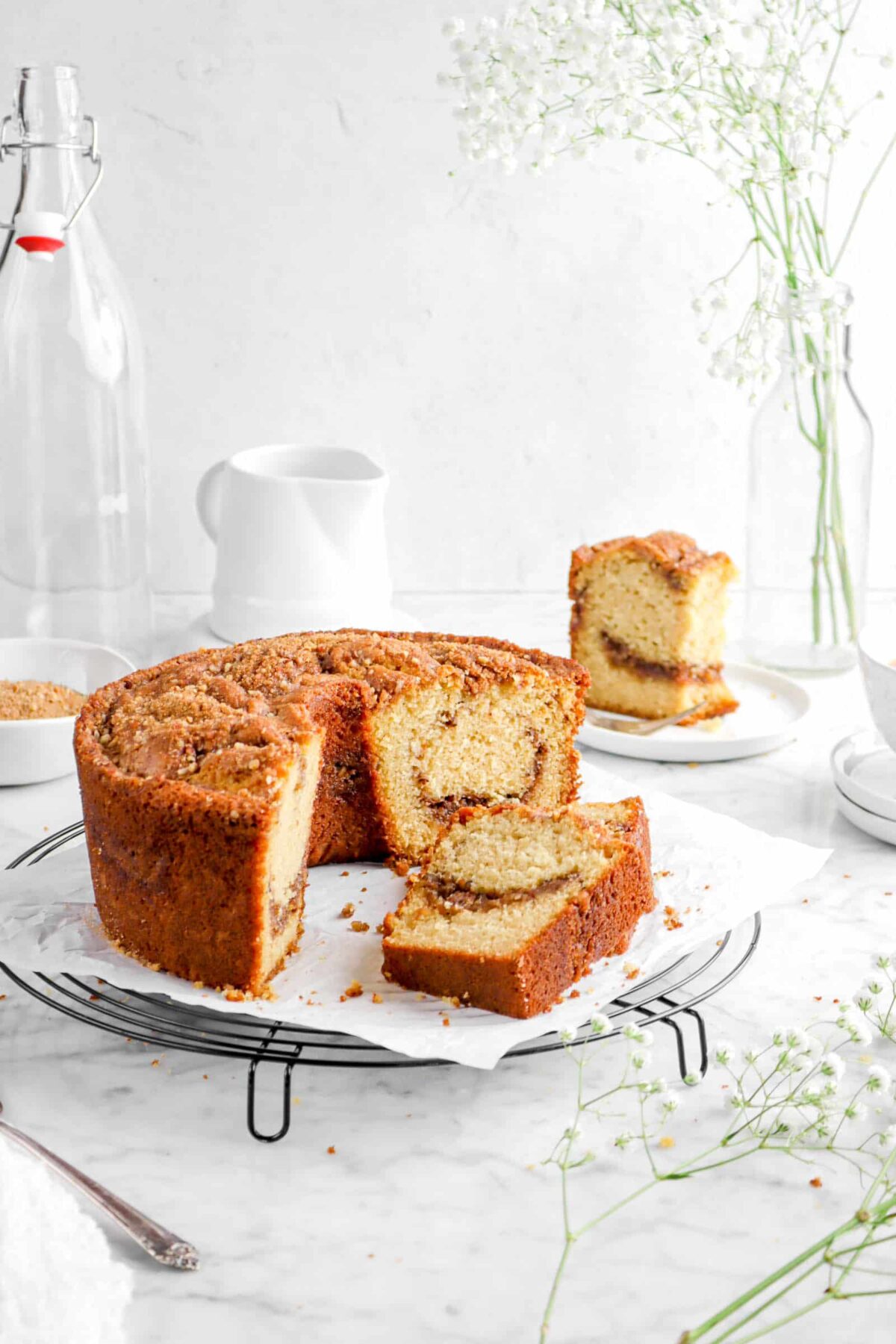coffee cake with a slice of cake behind, flowers, and a cheese cloth around cake