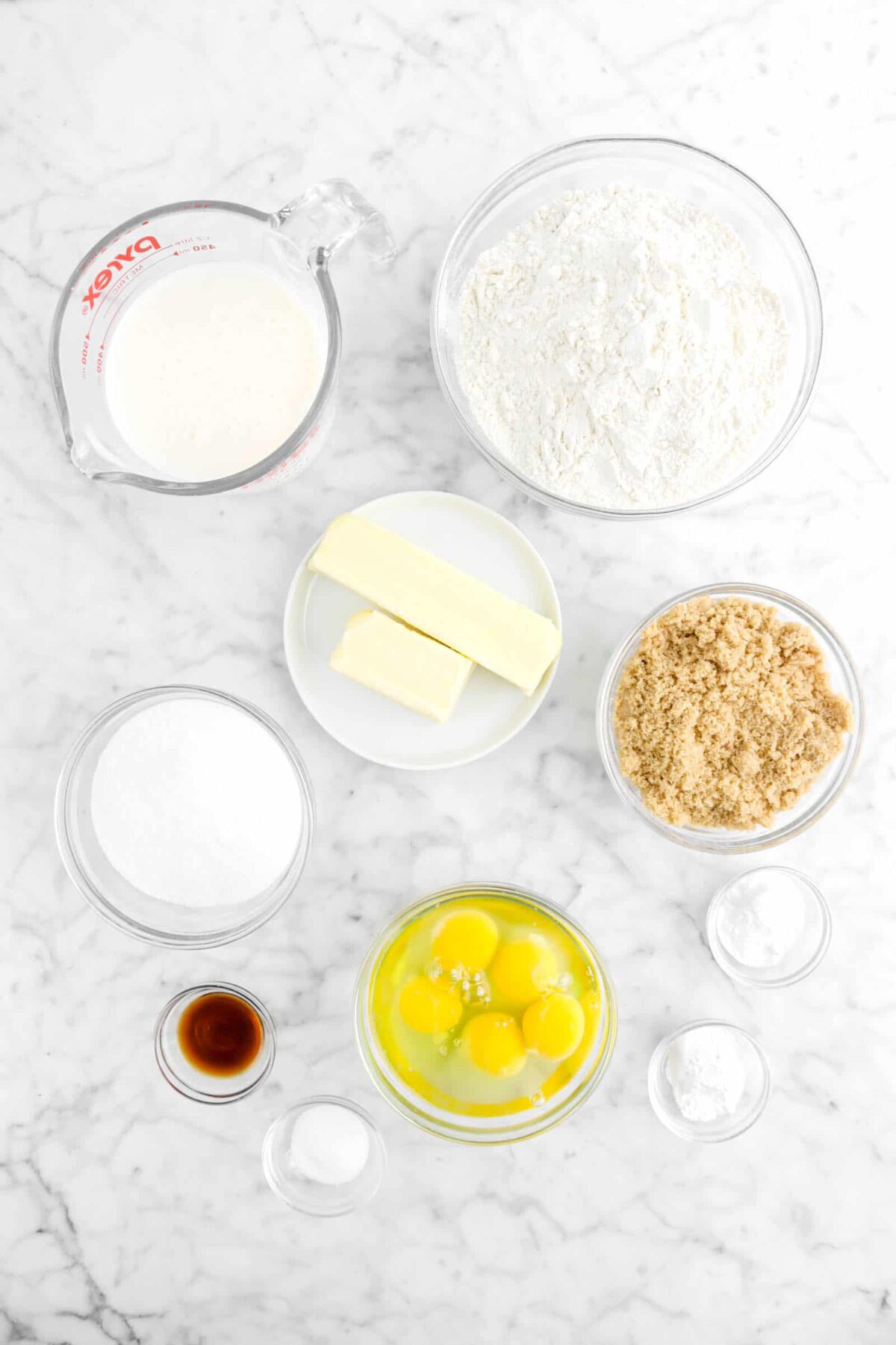 flour, milk, butter, brown sugar, white sugar, eggs, baking powder, baking soda, salt, and vanilla on marble counter