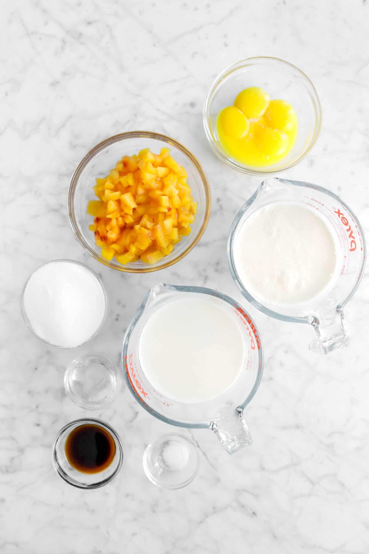 egg yolks, chopped peaches, heavy cream, whole milk, sugar, corn syrup, vanilla, and salt on a marble counter
