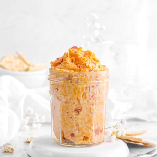 pimento cheese in a jar on a white plate with crackers and flowers around