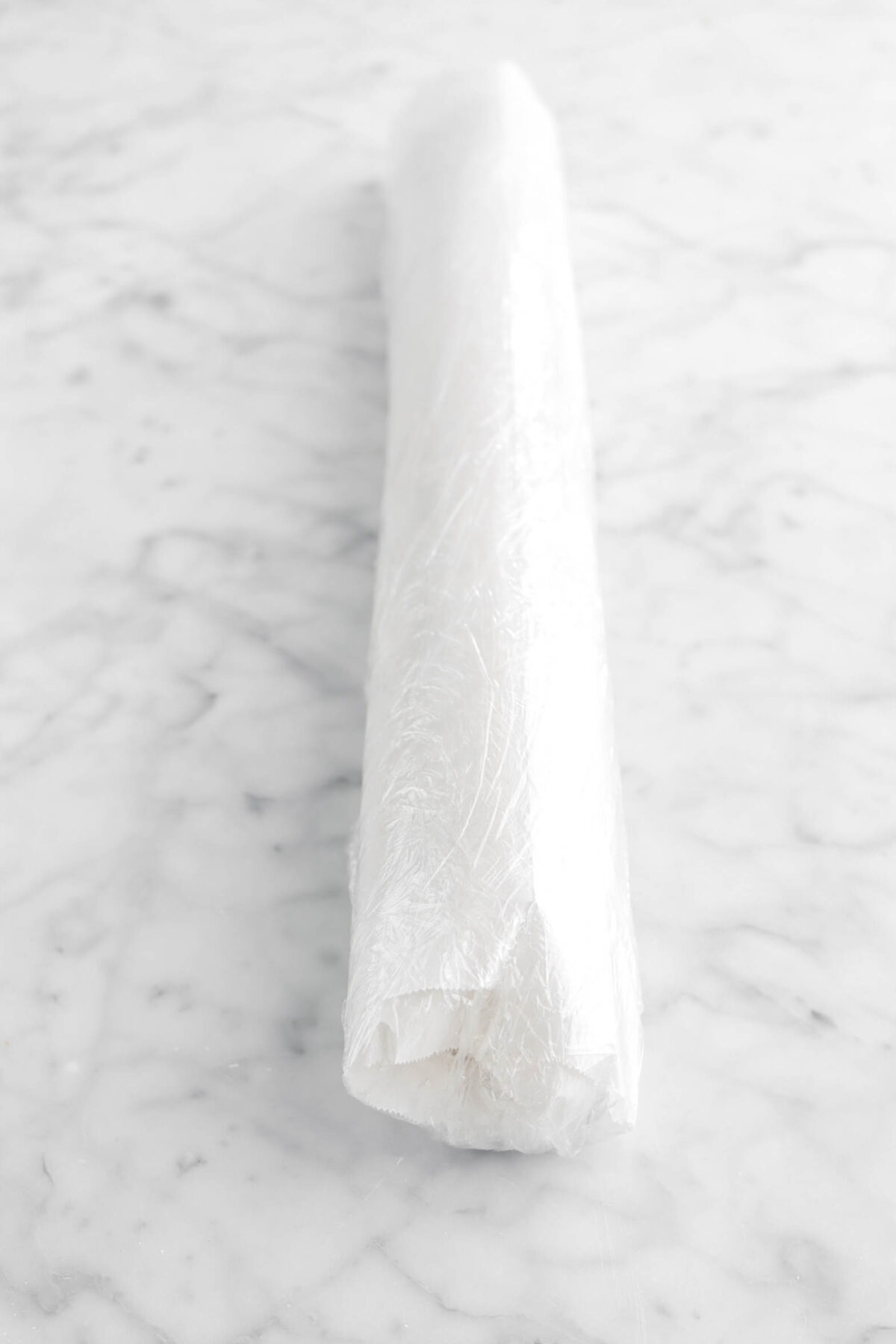 cookie dough log wrapped in parchment paper and plastic wrap on marble surface
