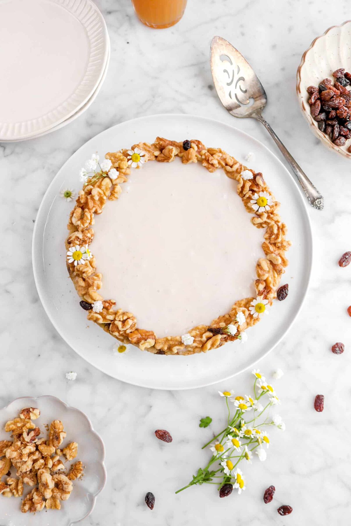 overhead shot of apple cake on white plate with raisins, walnuts, and flowers