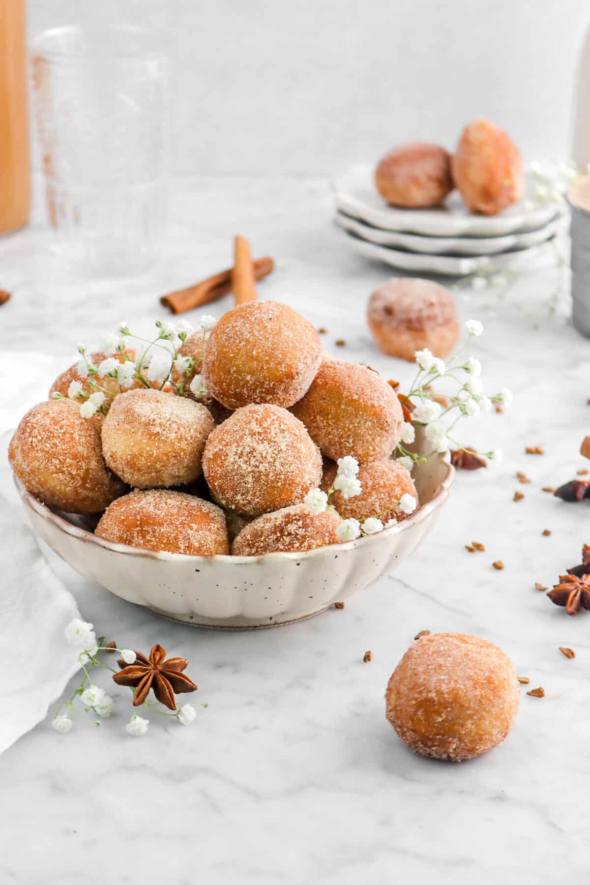 donut holes in bowl with more around, flowers, and star anise around