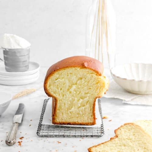 brioche on wire serving tray with crumbs around, a knife, and a slice in front