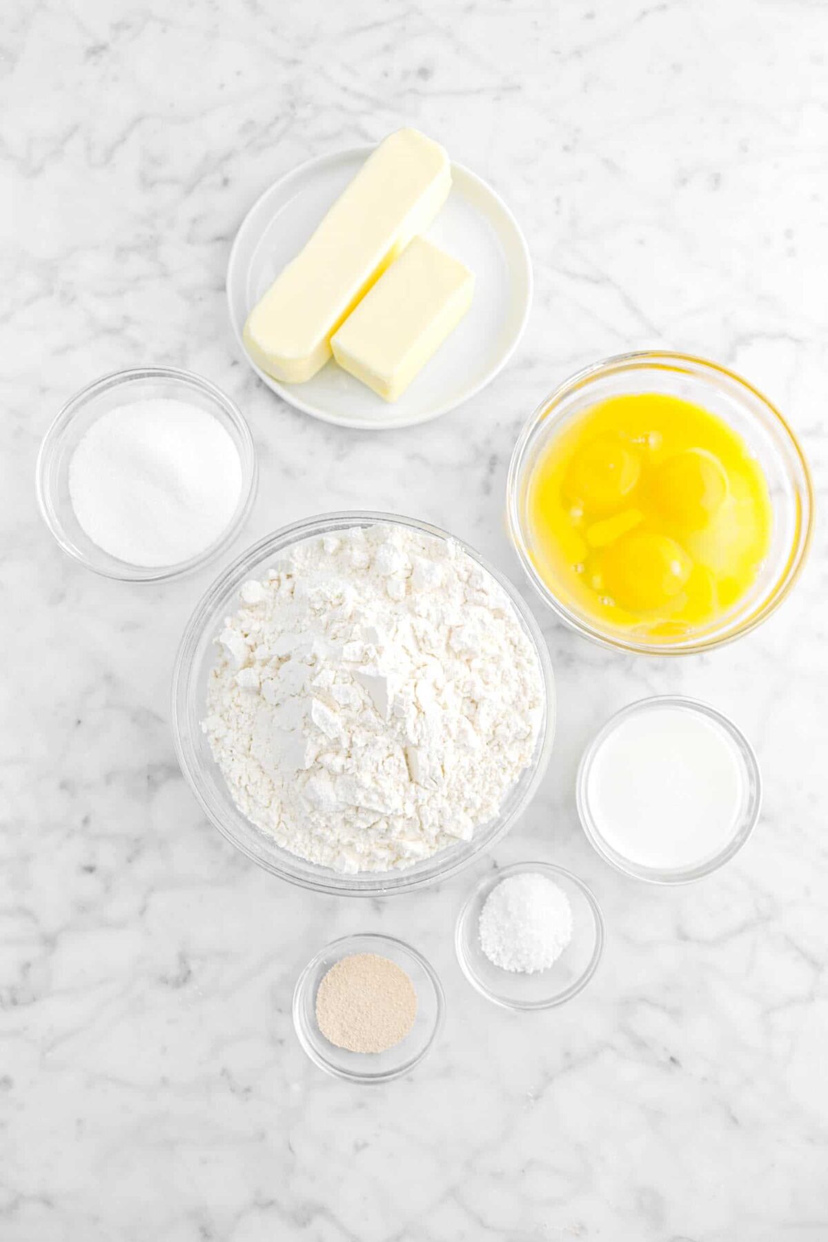butter, sugar, eggs, flour, milk, salt, and yeast on marble counter