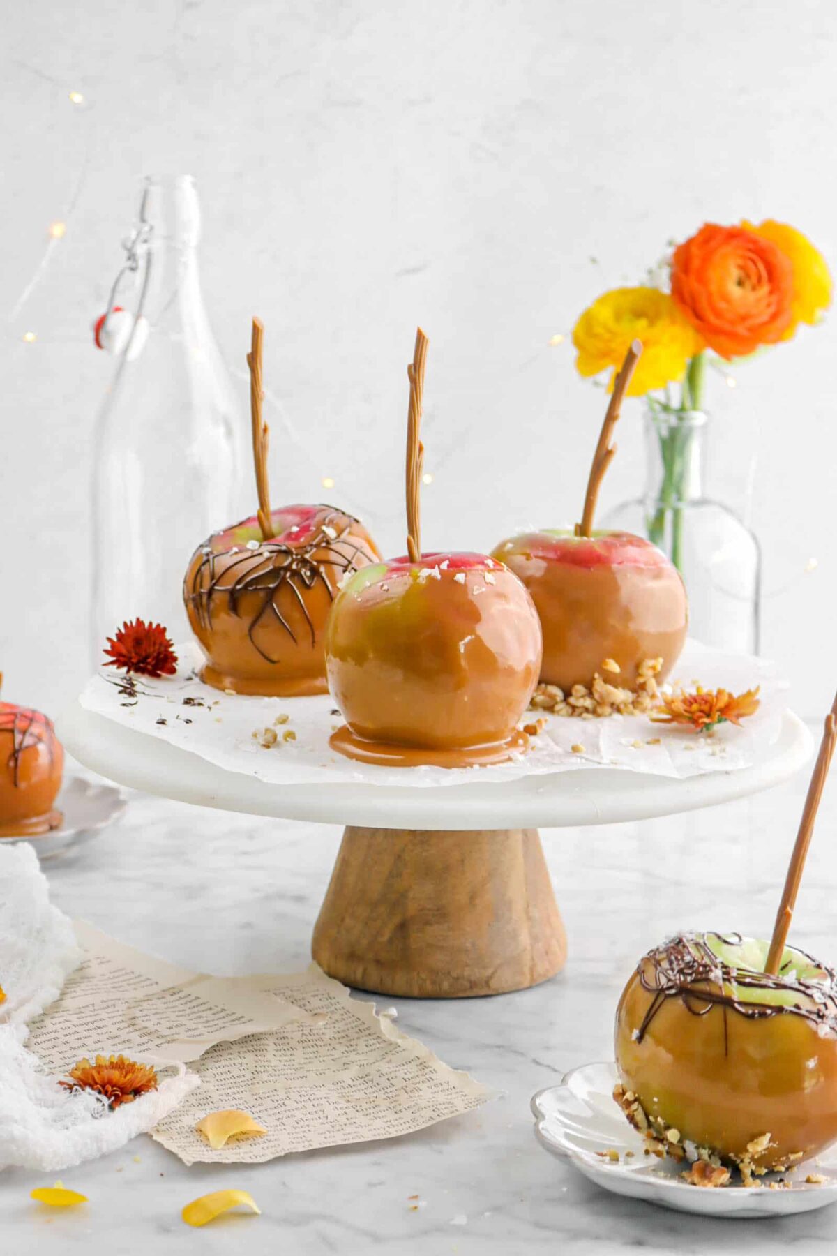 three caramel apples on marble cake plate with another caramel apple on a palte in front