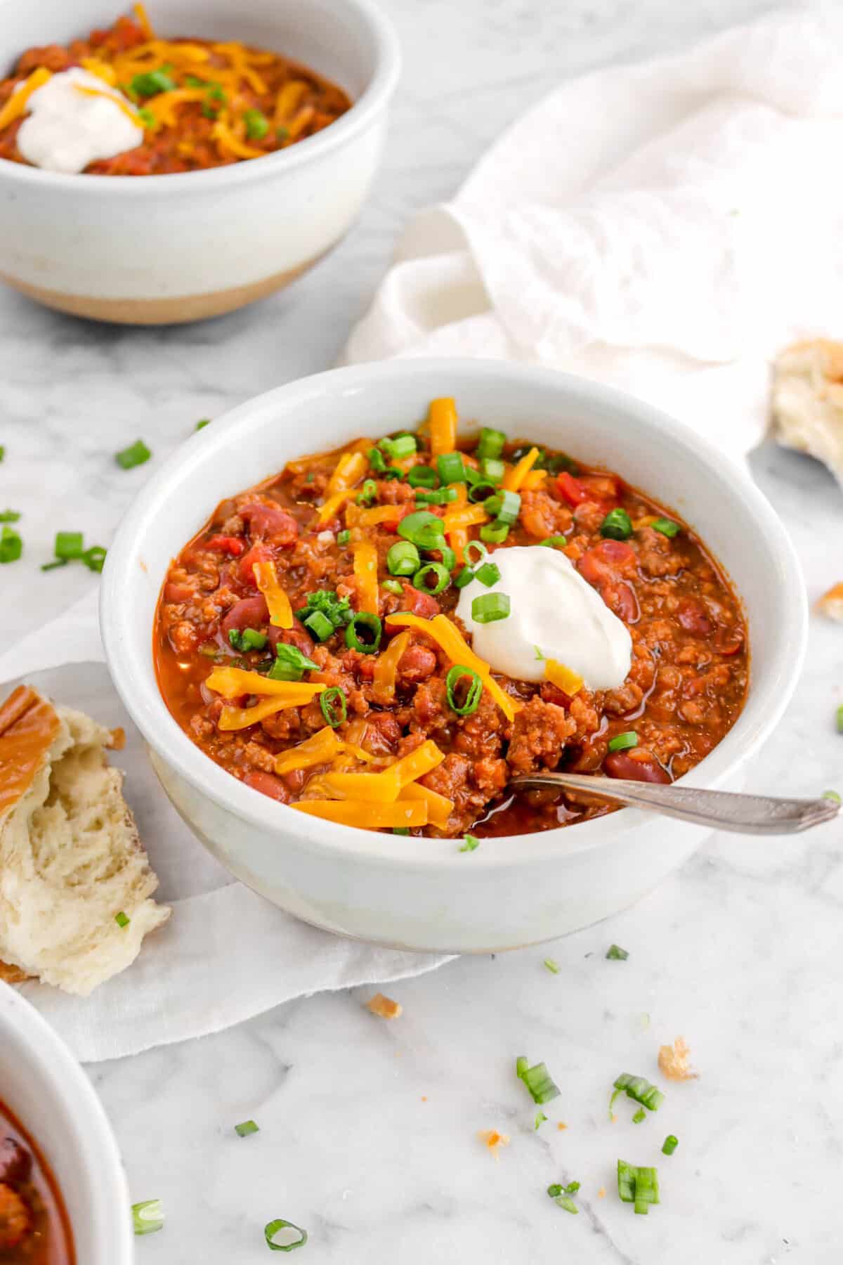 bowl of chili on white napkin with bread chunk beside and a bowl of chili behind