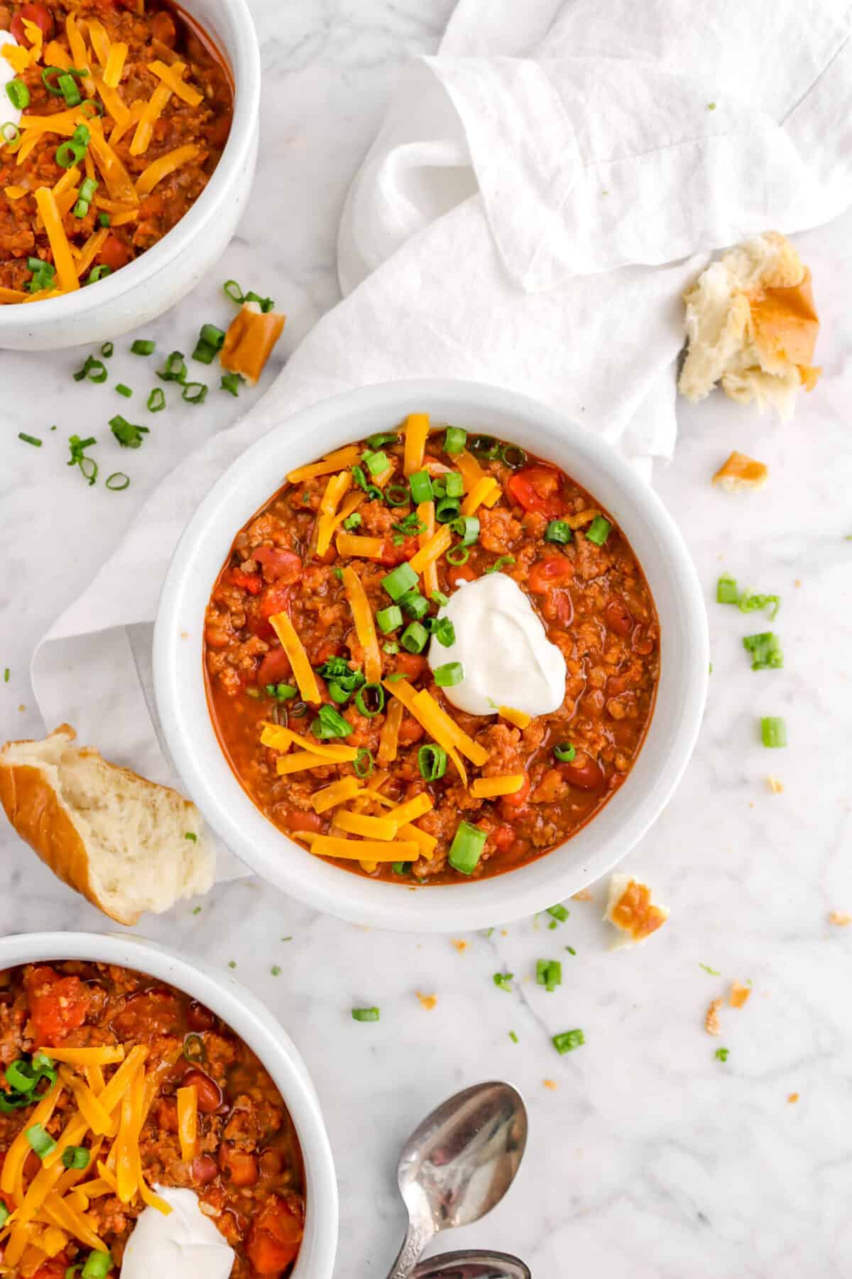 overhead shot of chili with bread, green onions, sour cream, and cheese