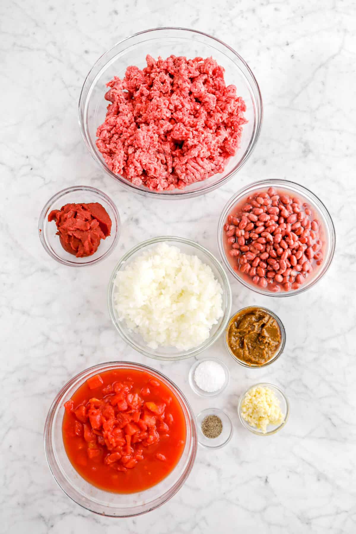 ground beef, red beans, tomato paste, chopped yellow onion, chili paste, salt, pepper, garlic, and tomatoes on marble counter