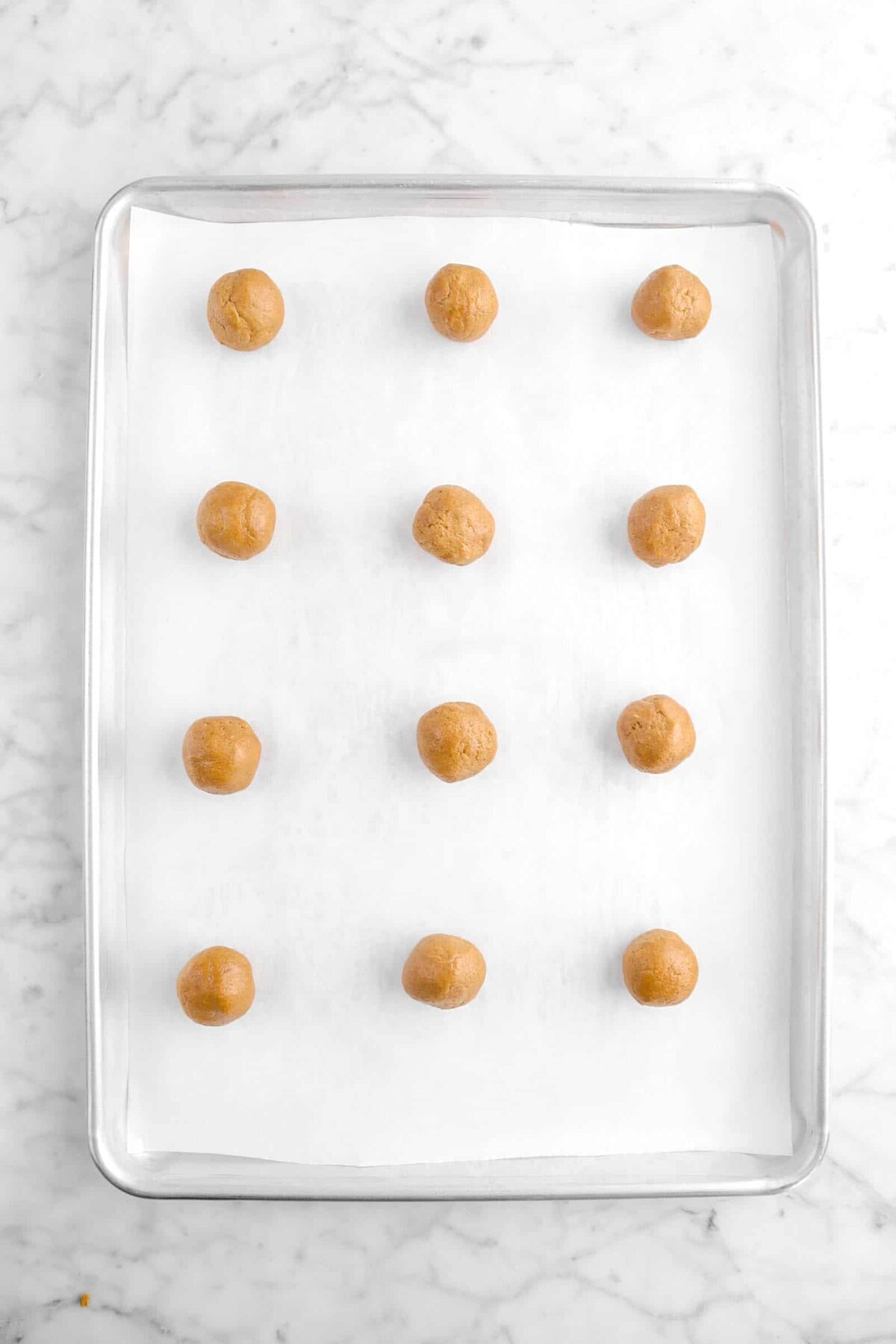 twelve cookie dough balls on lined cookie sheet