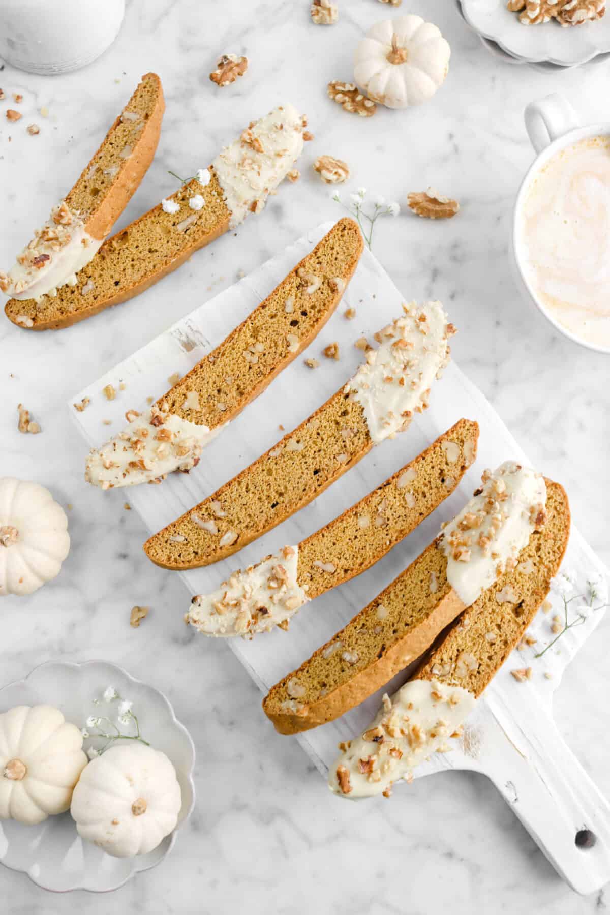 five biscotti on wood serving board with pumpkins, flowers, and walnuts, with two biscotti laying in front of the board