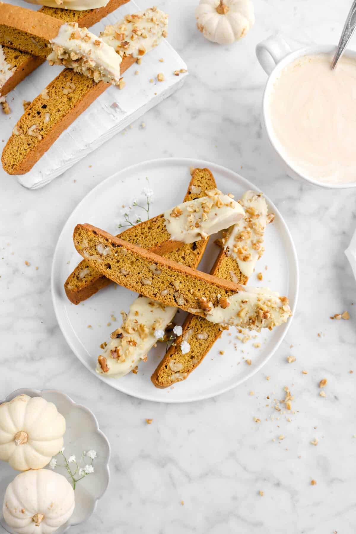overhead shot of four pumpkin biscotti on white plate with coffee and three mini pumpkins
