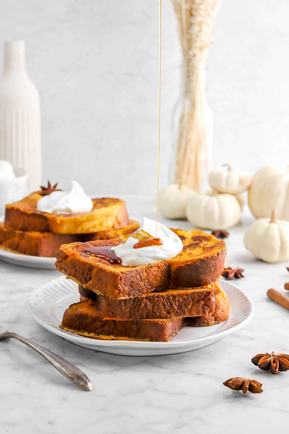 three stacked pumpkin french toasts on white plate with maple syrup being poured on it