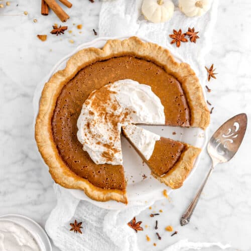 pumpkin pie cut with slice still in pie with whole spices and mini pumpkins around