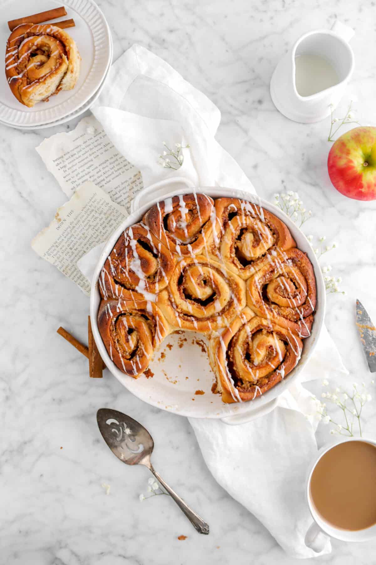 overhead of apple cinnamon rolls on white napkin with one missing from the pan