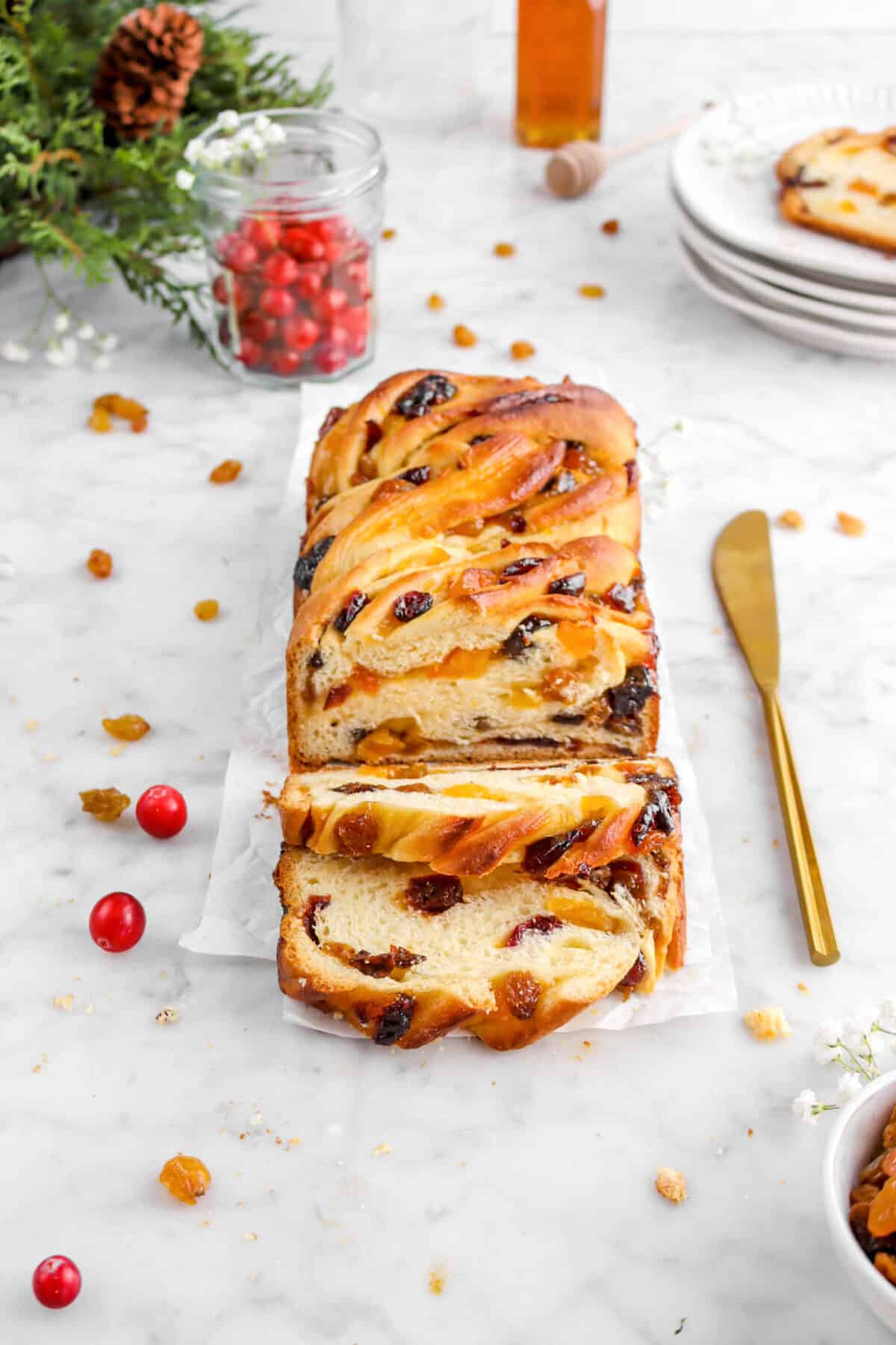 babka on parchment paper with cranberries, gold knife, golden raisin, and greenery