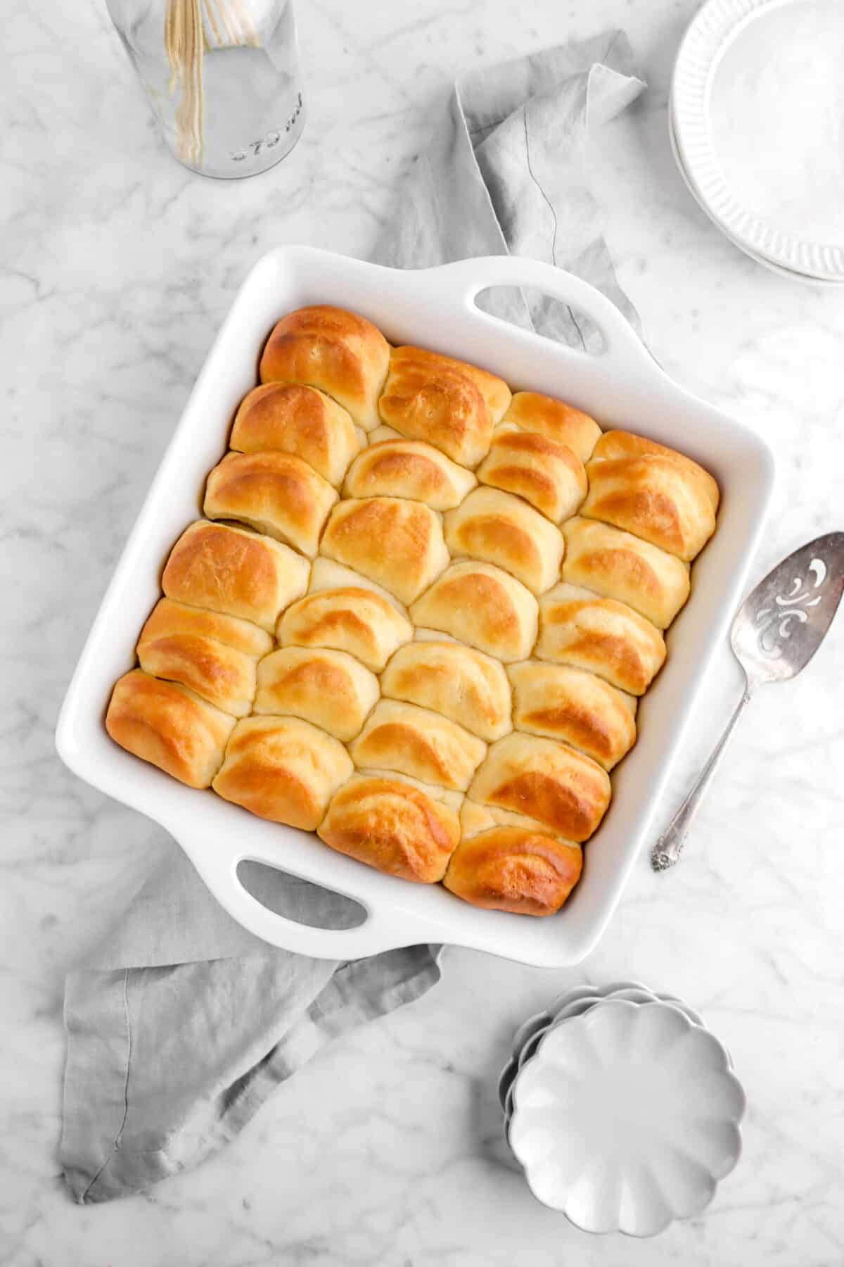 square casserole of rolls on grey towel with plates and cake knife