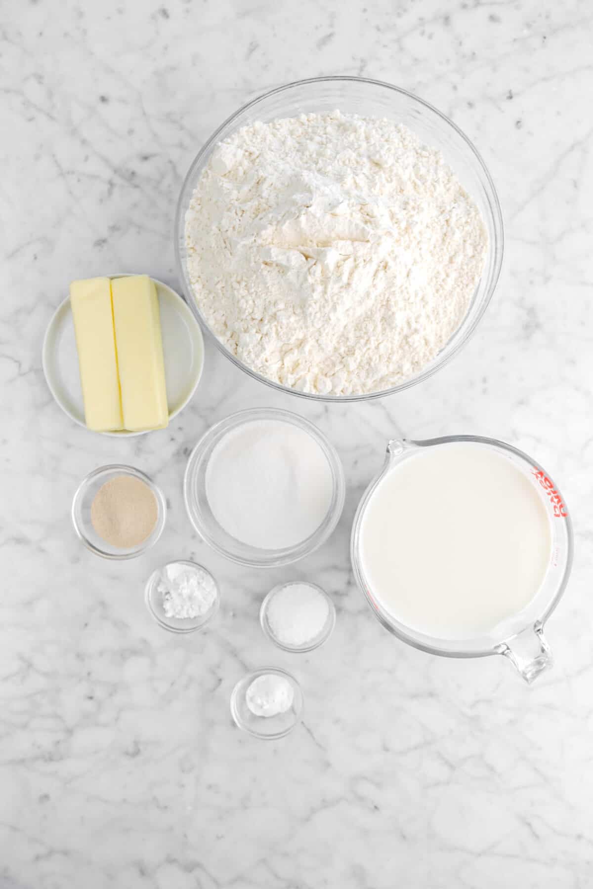flour, butter, sugar, yeast, milk, salt, baking powder, and baking soda on marble counter