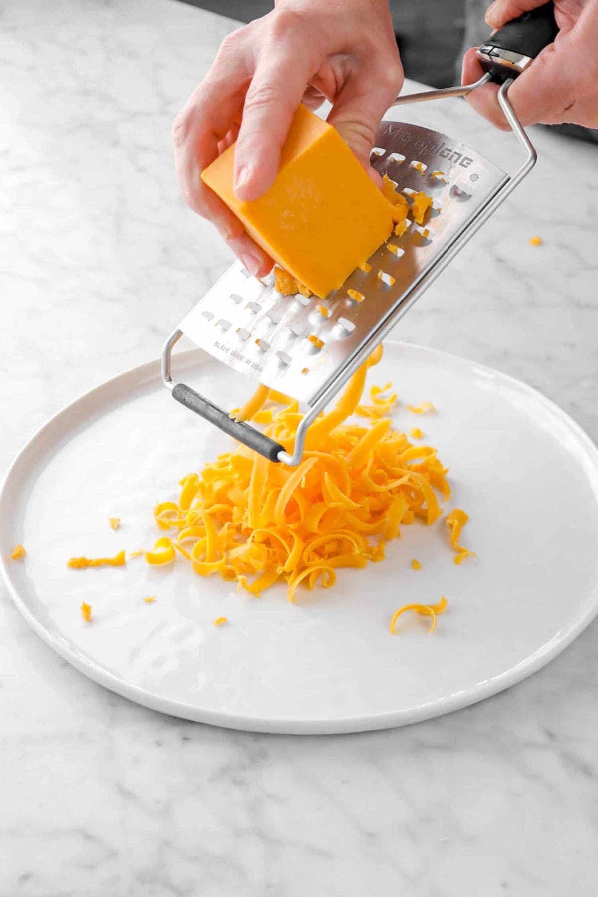 cheddar cheese being grated onto white plate