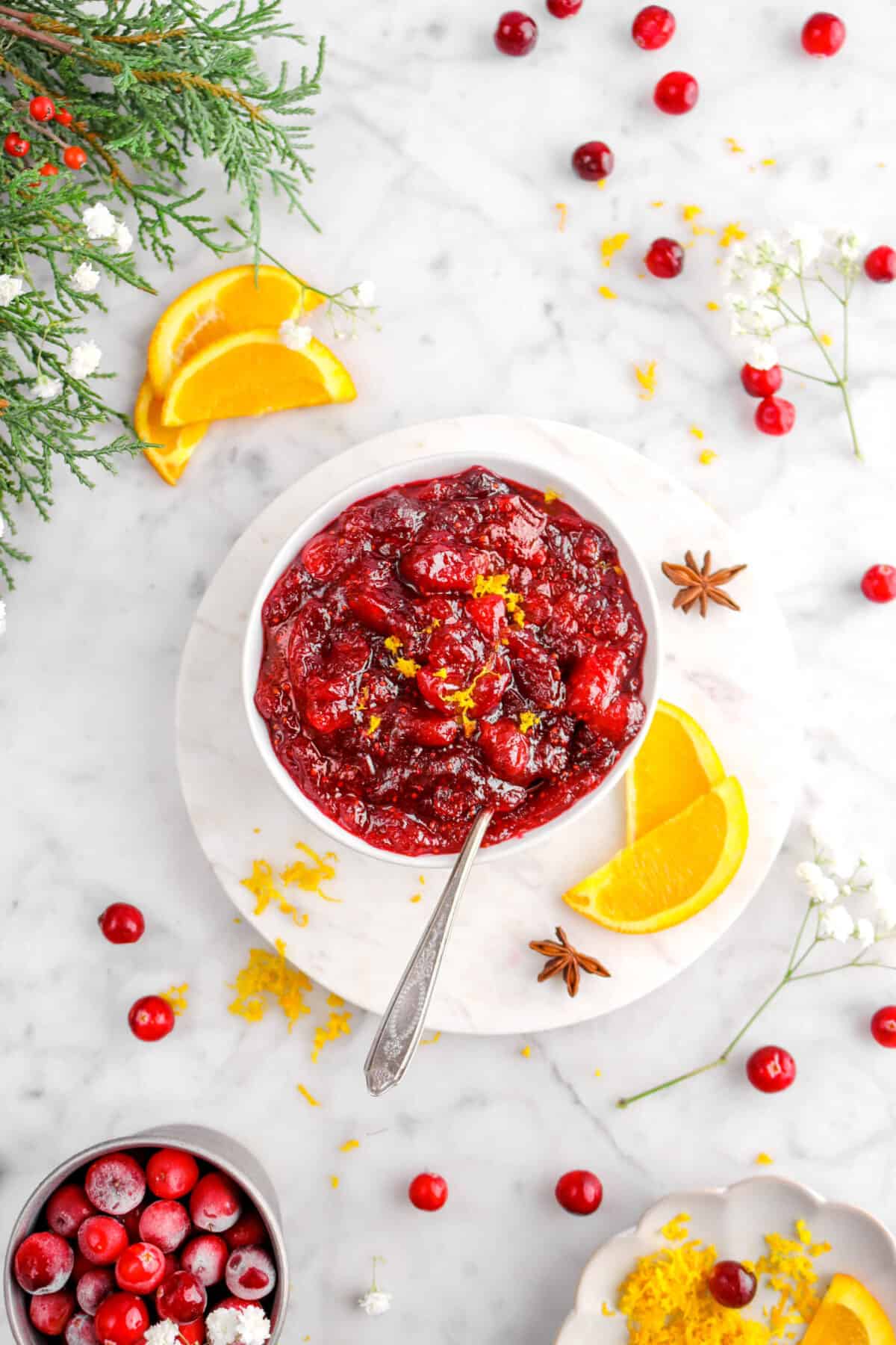 cranberry sauce in white bowl with spoon dug in with orange slices, fresh cranberries, and flowers