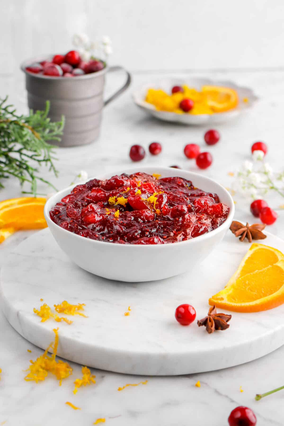 cranberry sauce in white bowl with zest, fresh cranberrries, and orange slices around