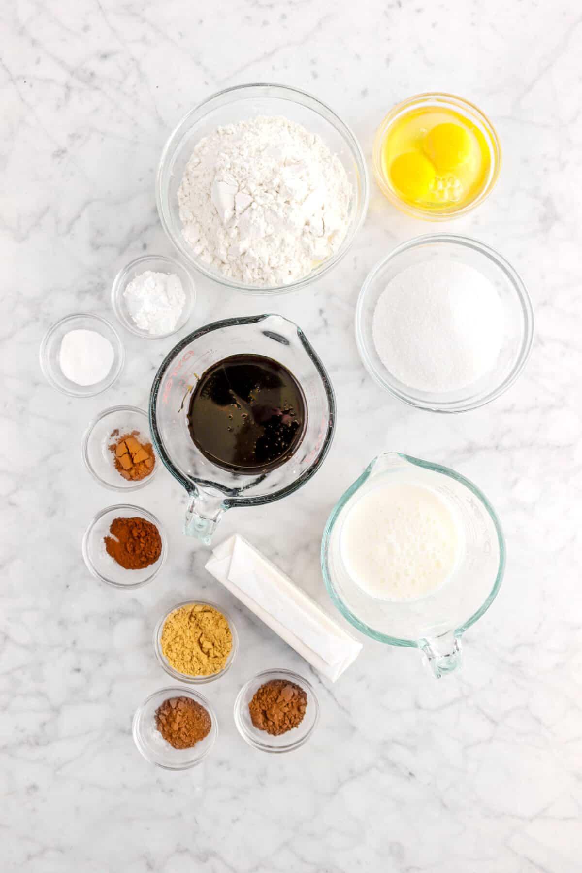 flour, eggs, baking soda, baking powder, molasses, sugar, heavy cream, butter, ground ginger, allspice, cloves, cinnamon, and nutmeg on marble counter