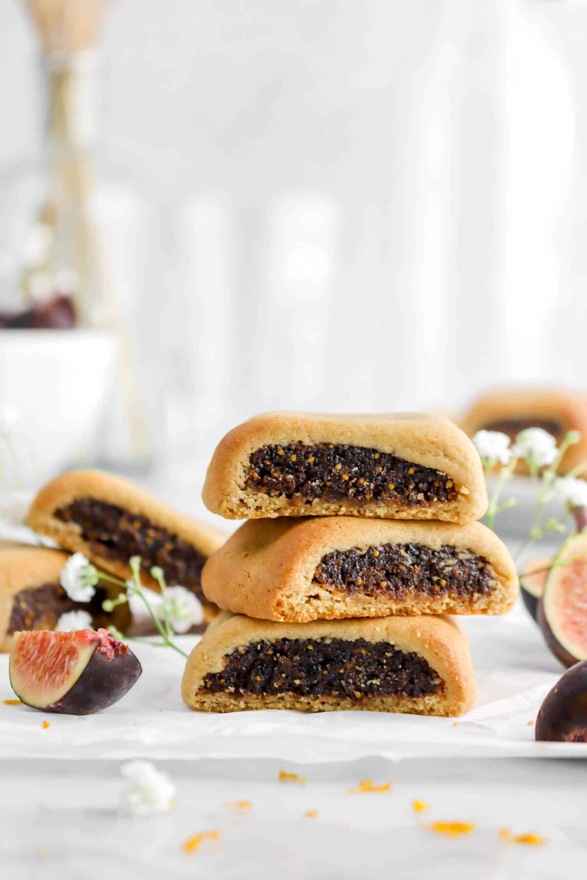 close up of three stacked fig newtons on parchment paper with flowers and fresh figs