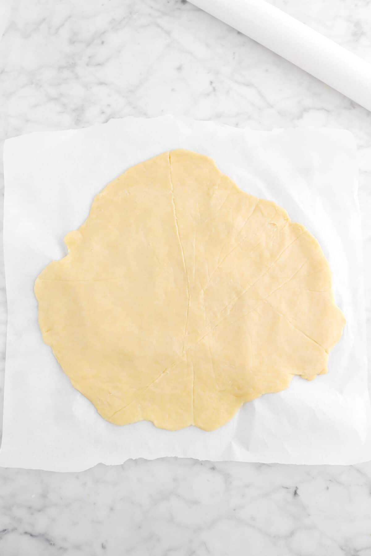 pie dough rolled out on parchment paper with white rolling pin