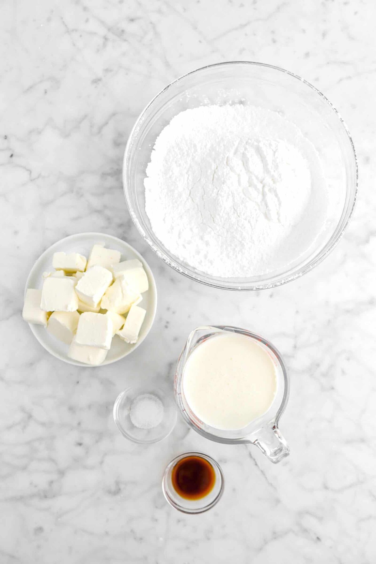 powdered sugar, cream cheese, heavy cream, salt, and vanilla on marble counter.