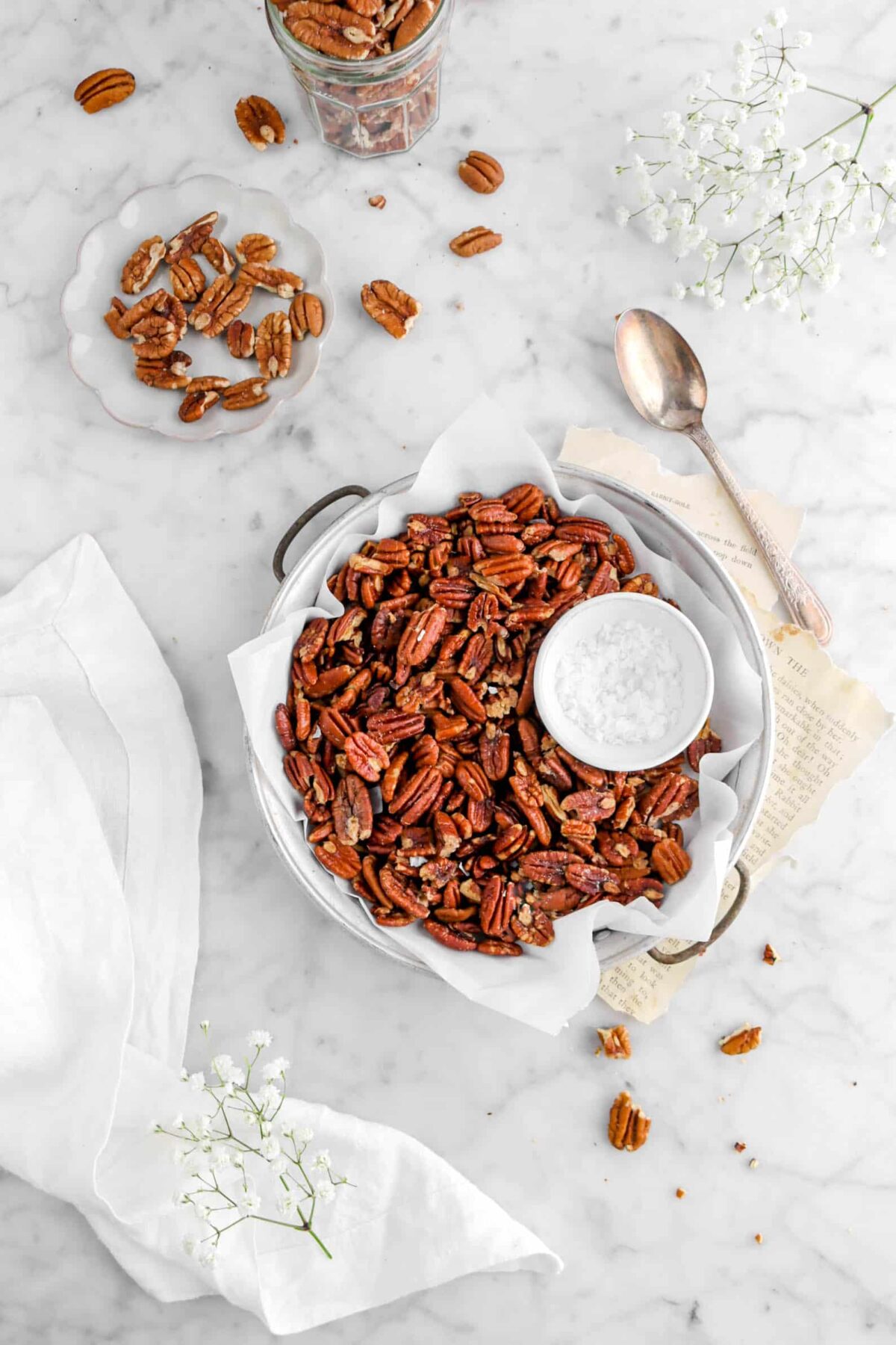 roasted pecans in vintage cake pan on top of book pages with unrated pecans around and flowers