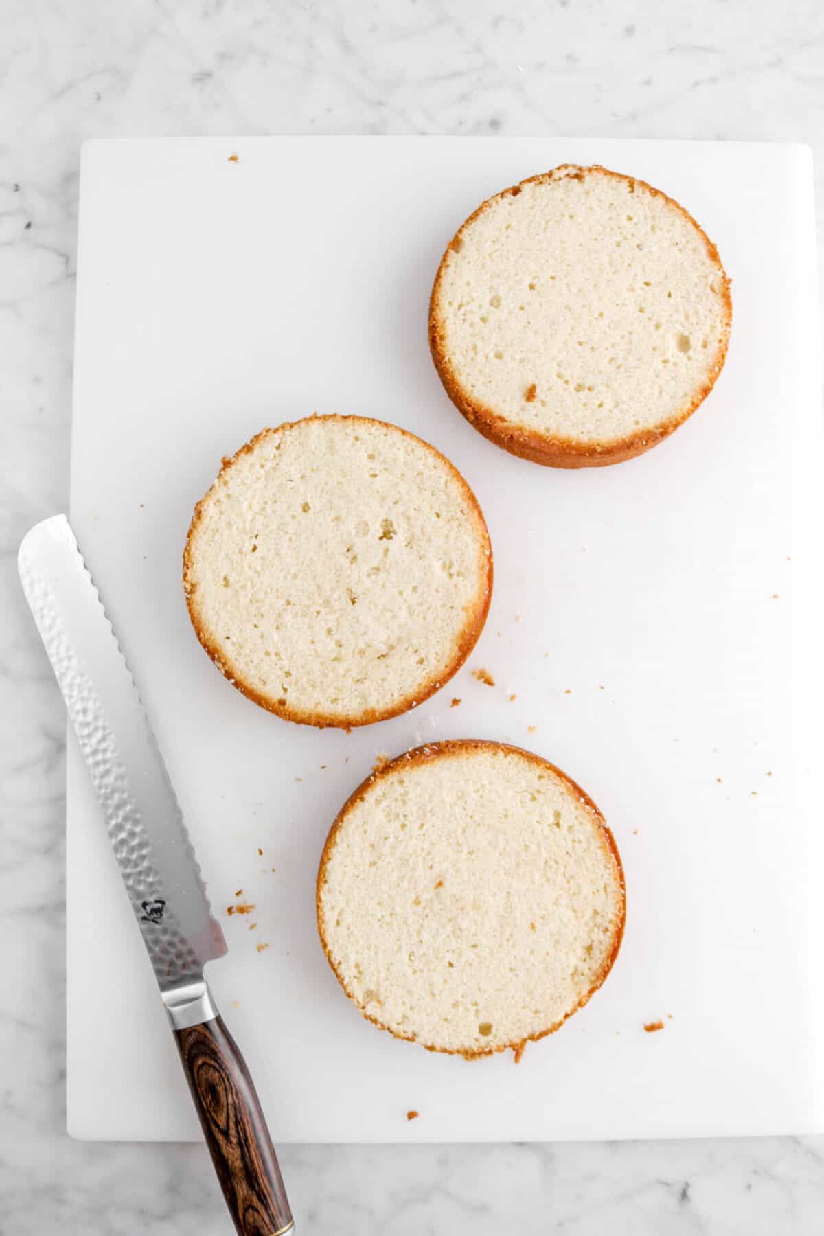 three round cakes with tops cut off on white cutting board