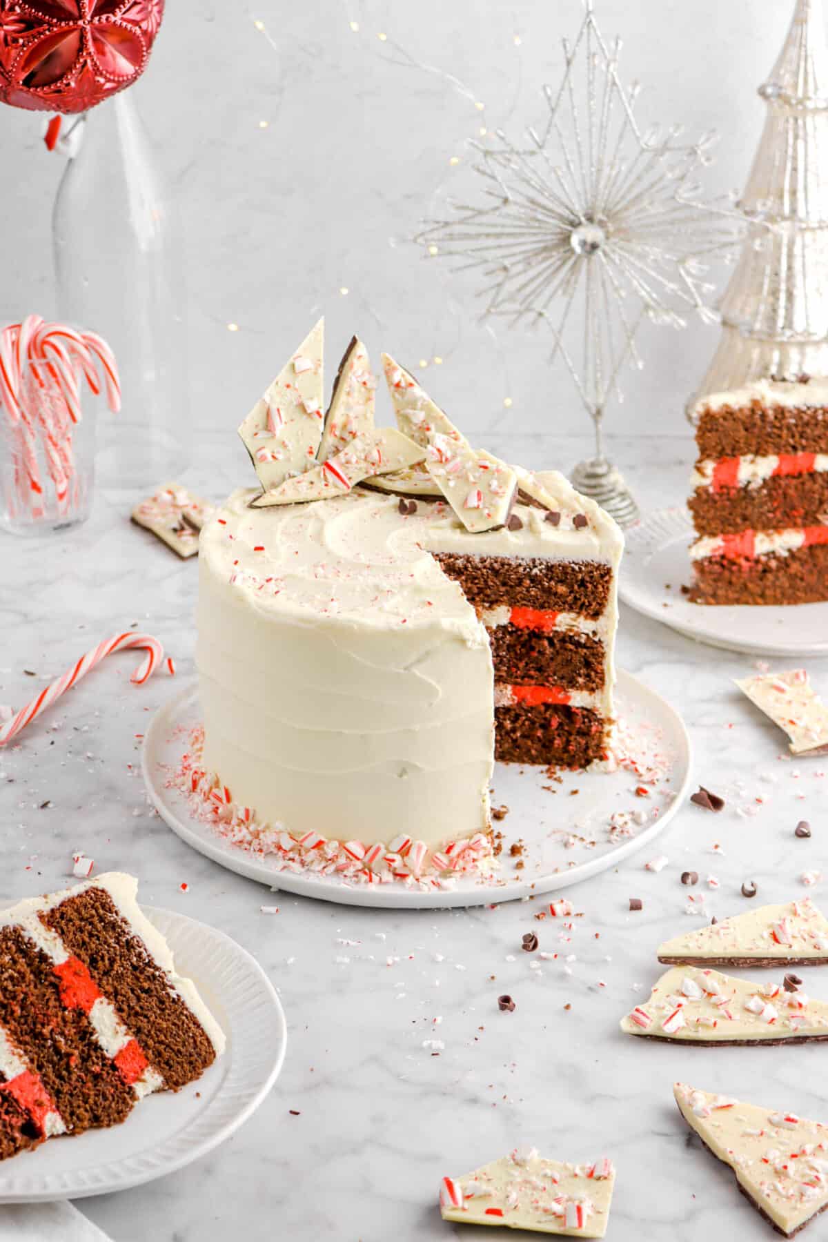chocolate peppermint cake with two slices on white plates with candy canes and peppermint bark