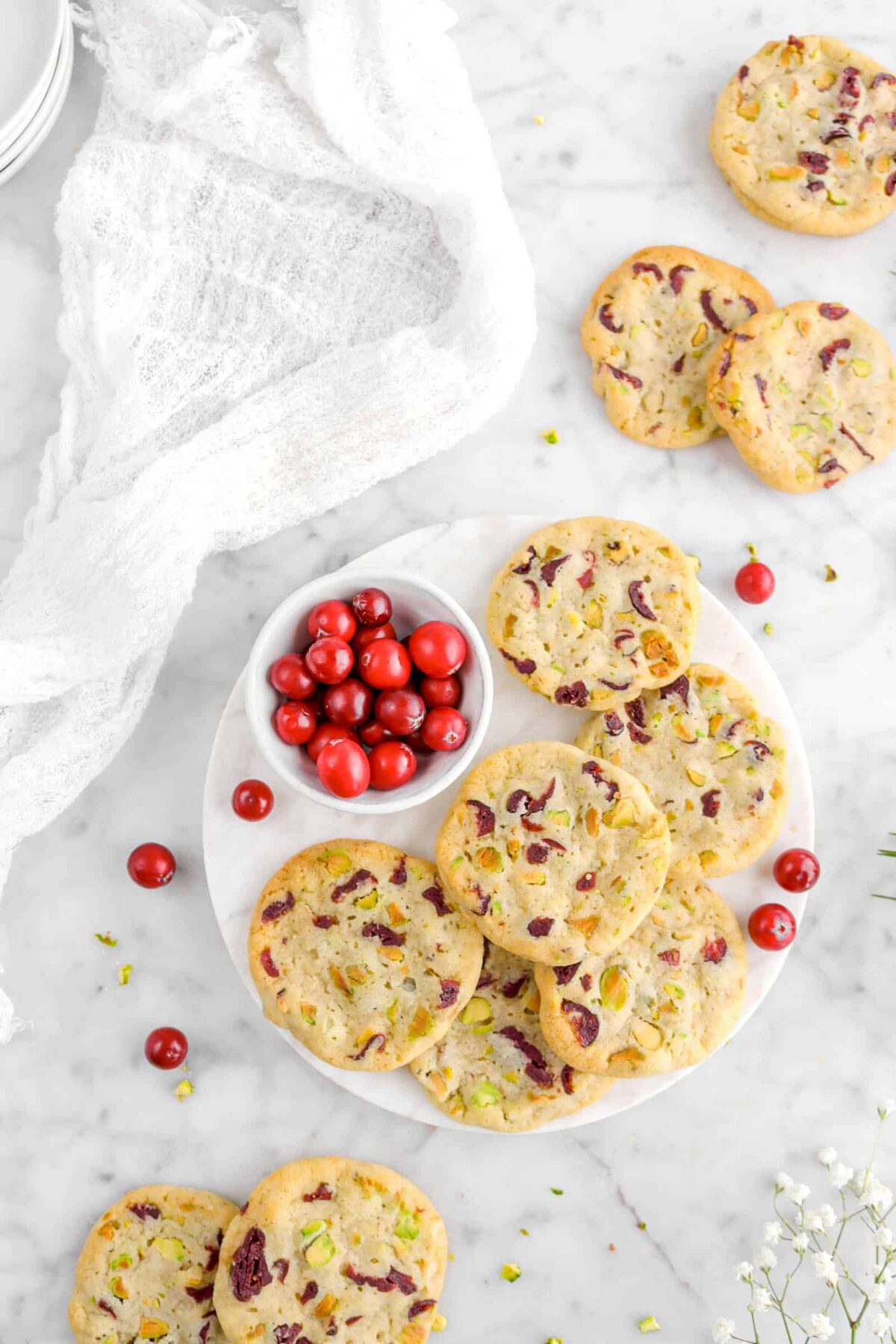 cookies on marble with bowl of fresh cranberries, white cheese cloth, and flowers
