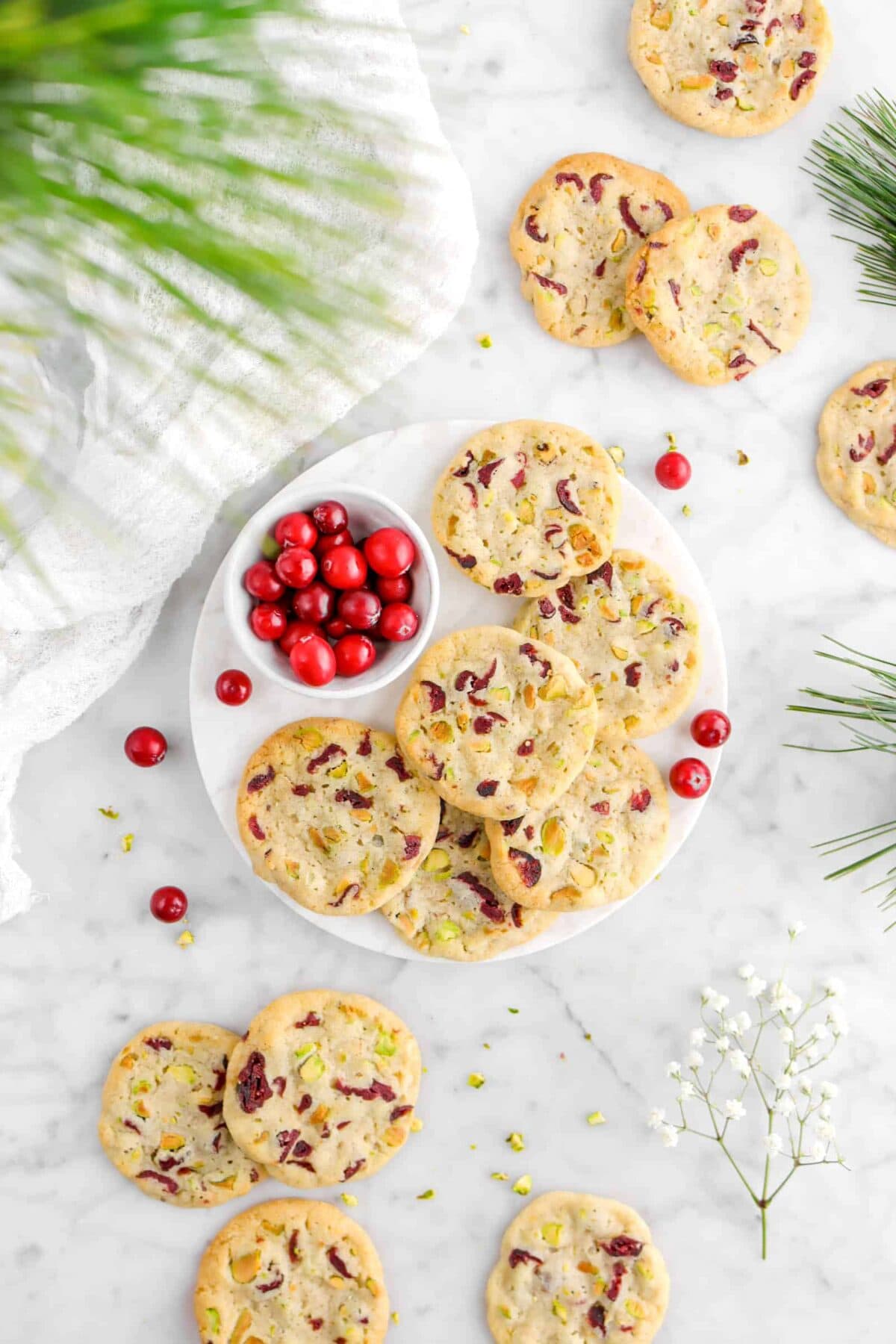 overhead photo with christmas greenery over cranberry pistachio cookies