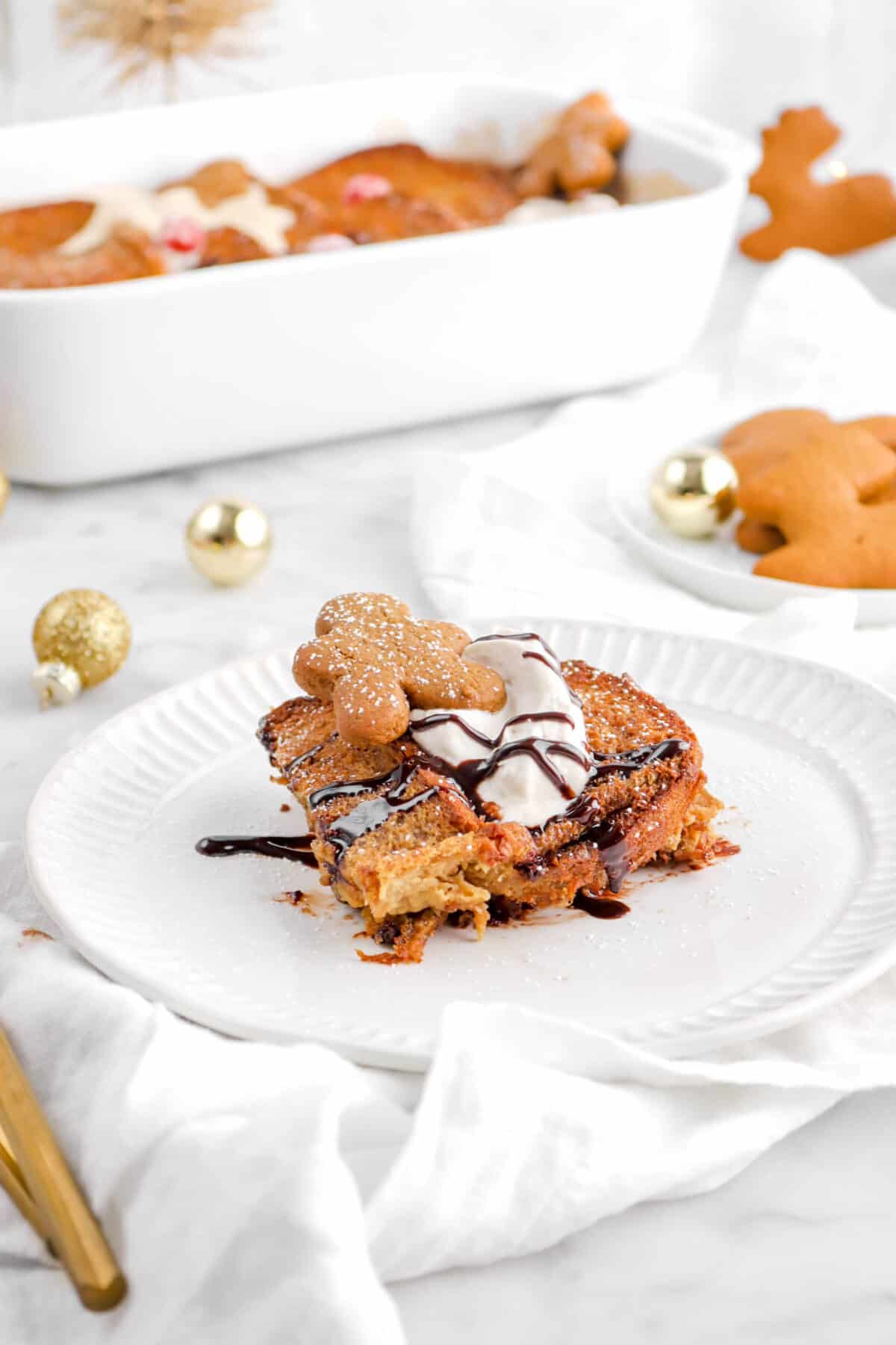 slice of gingerbread french toast on white plate with gold ornaments, cookies, and casserole behind