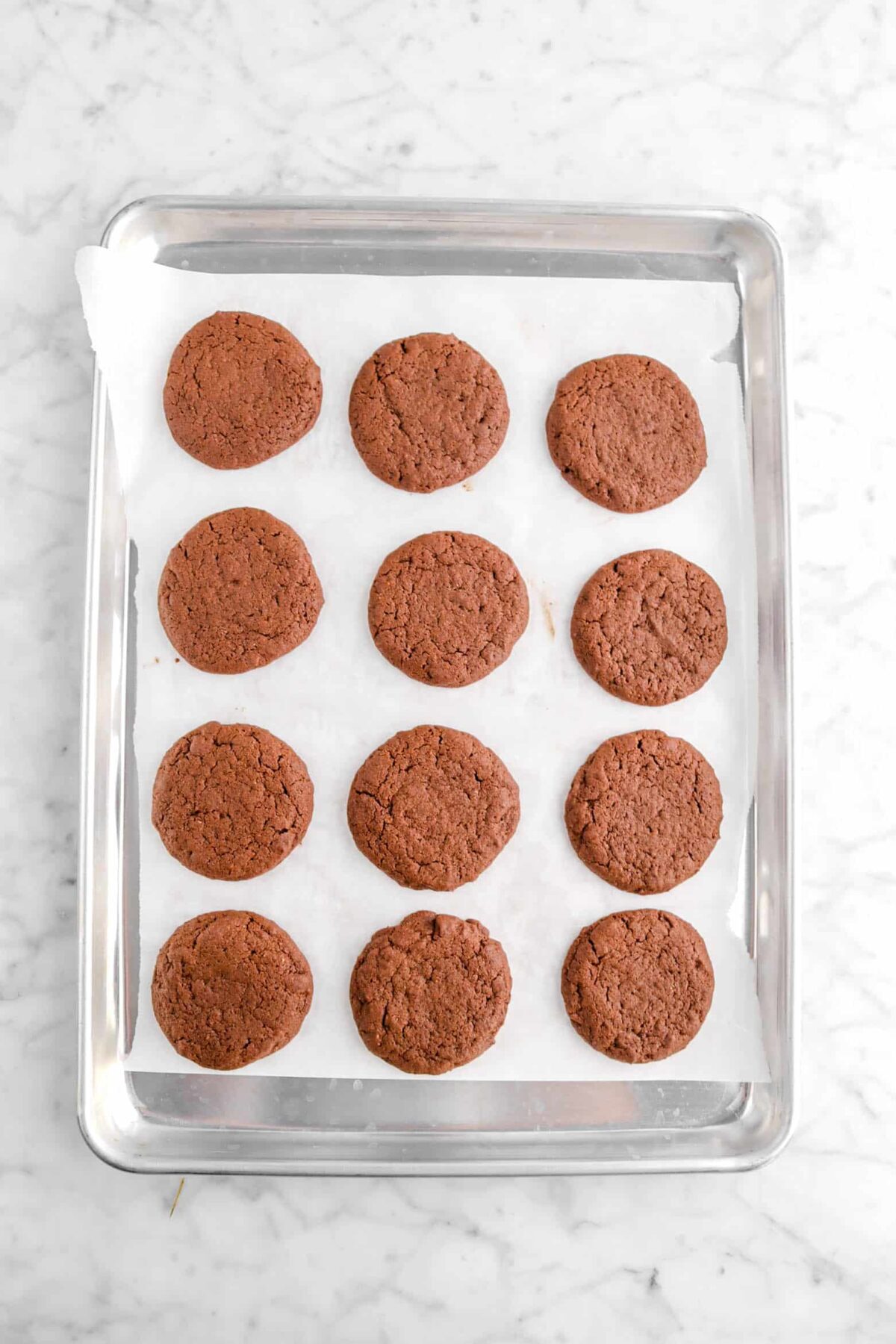 twelve baked chocolate cookies on lined sheet pan