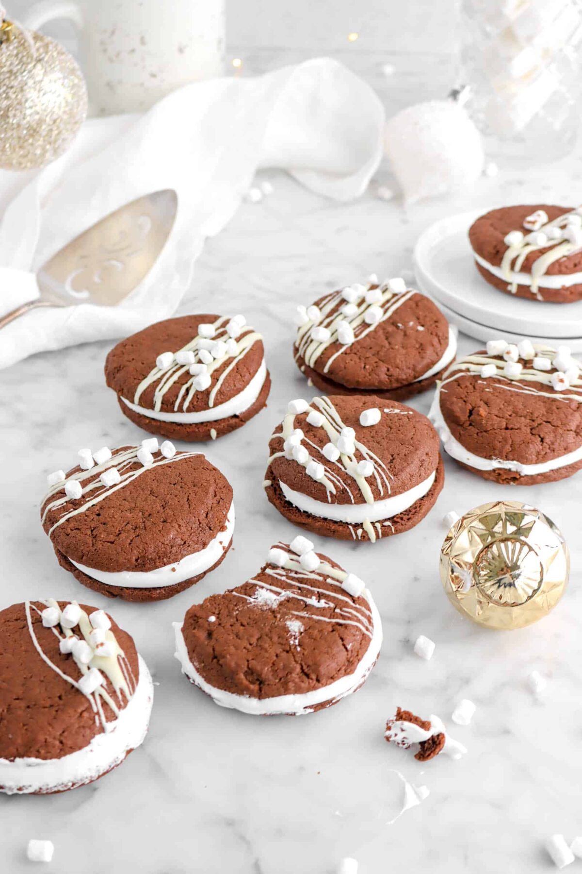 eight hot cocoa cookies on marble counter with mini marshmallows and gold ornaments
