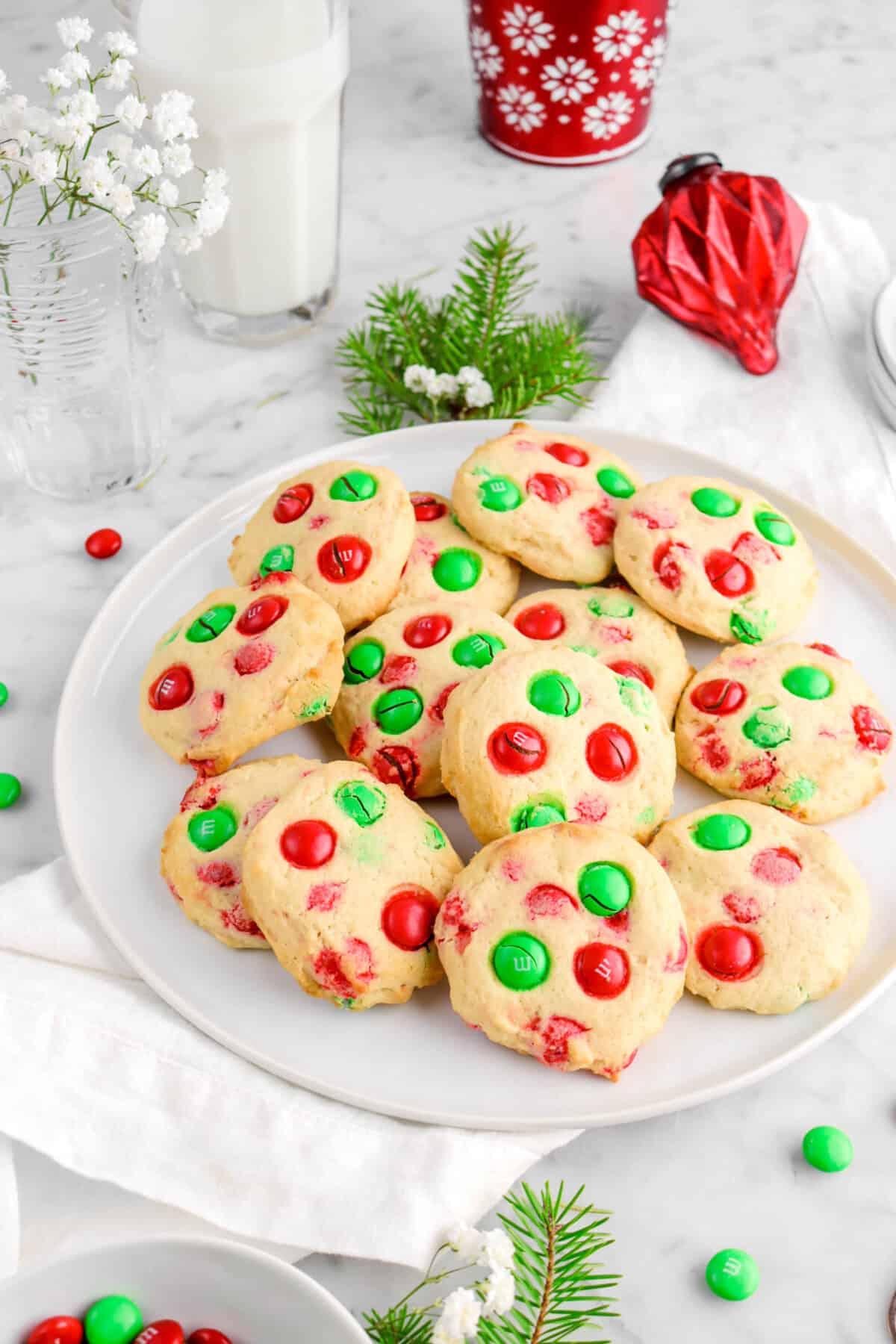 m*m cookies on white plate with red ornament, glass of milk, and greenery