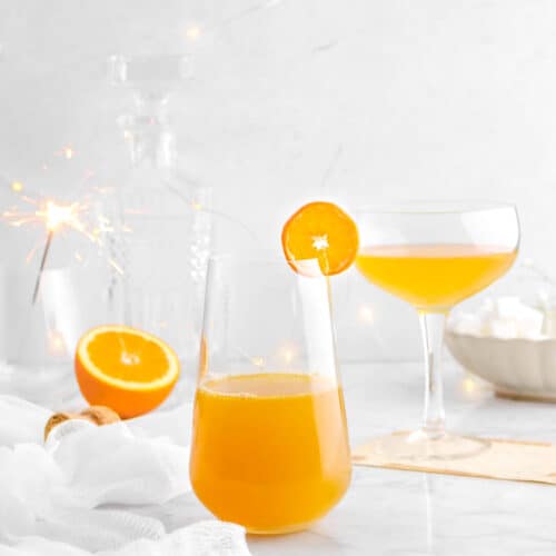 orange champagne cocktail with sparkler behind, fairy lights, and half of an orange