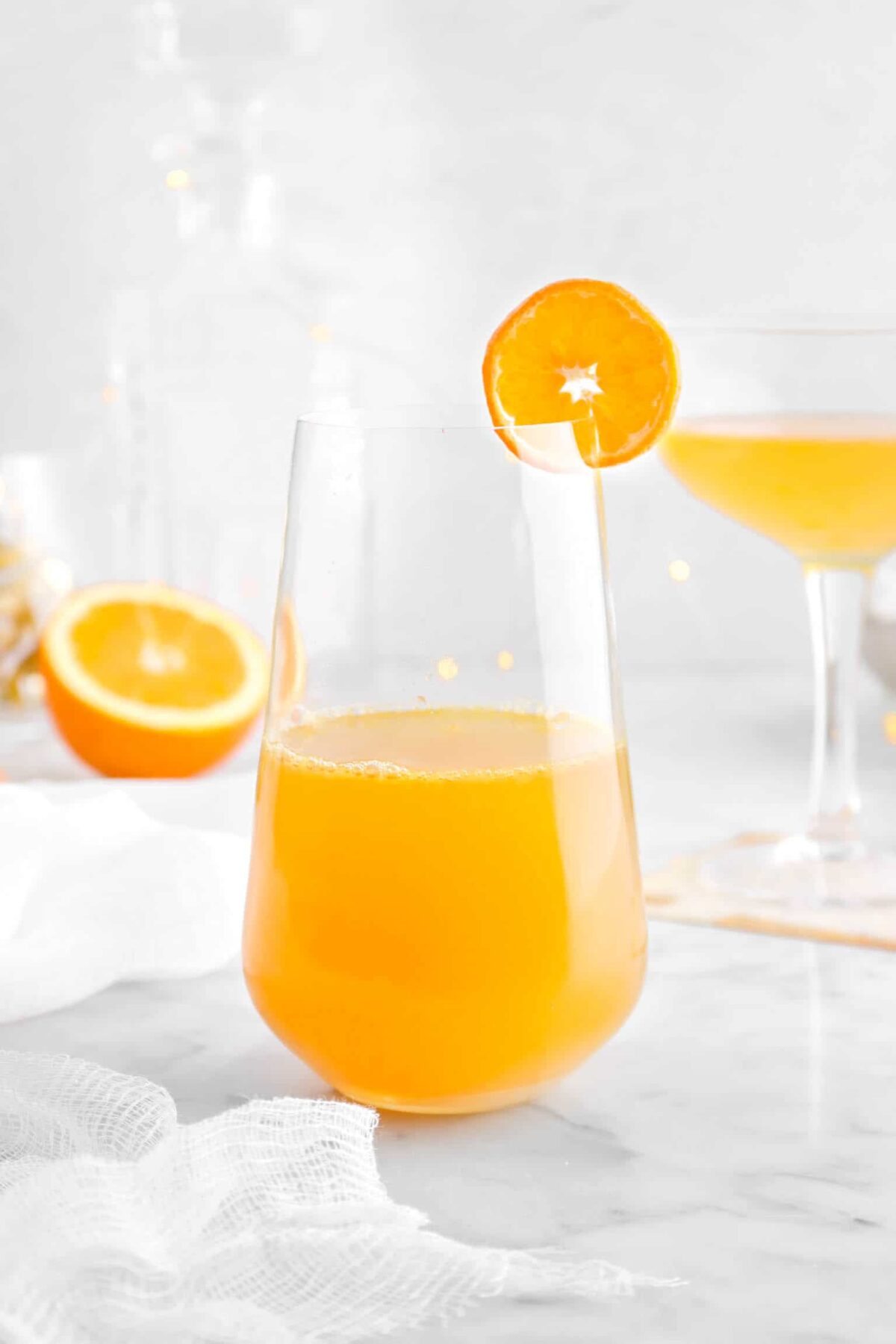 close up of champagne cocktail with mini orange slice and white cheese cloth