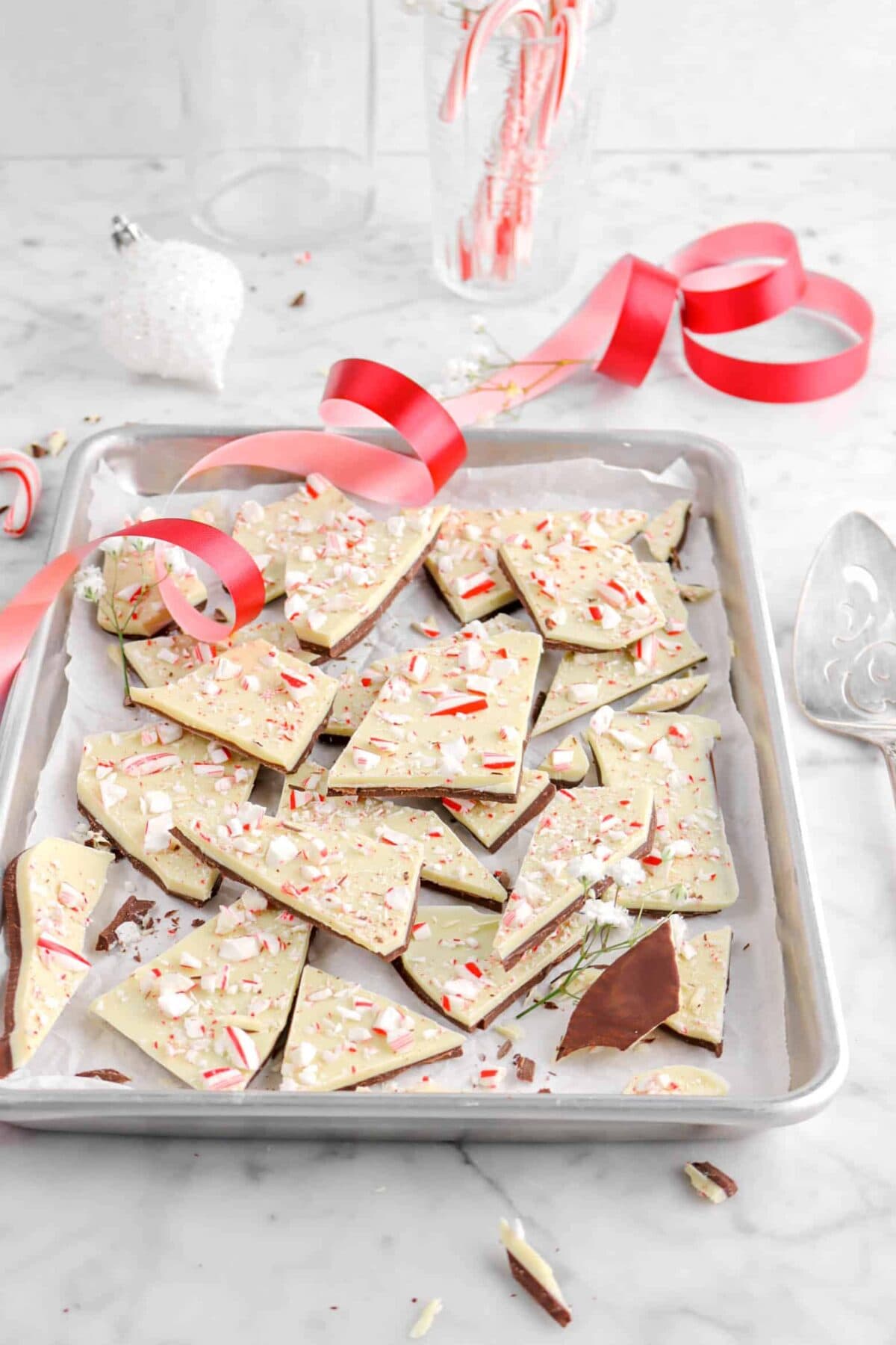 front shot of peppermint bark in sheet pan with red ribbon and white ornament