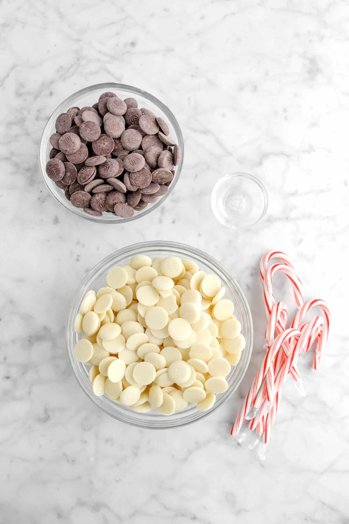 bowl of dark chocolate, bowl of white chocolate, peppermint oil in small bowl, and candy canes on marble counter