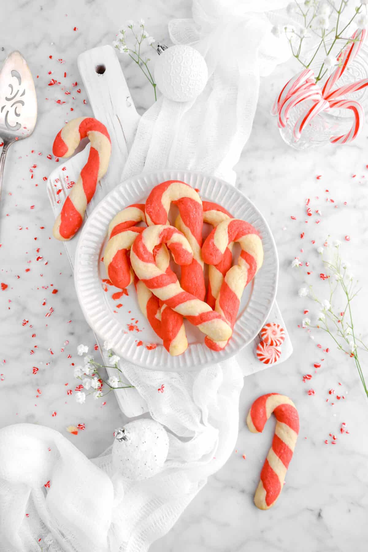 plate full of candy cane cookies with white napkin, two candy cane cookies beside, and crushed peppermint around