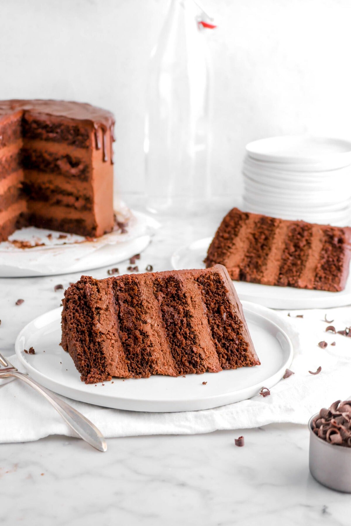 two slices of chocolate cake on white plates with cake behind